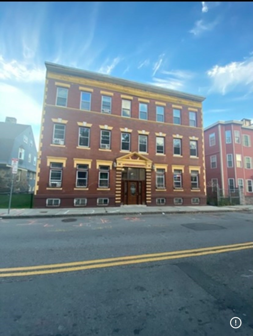 Three-story red-brick apartment building with cream trim and a central entrance facing the street.