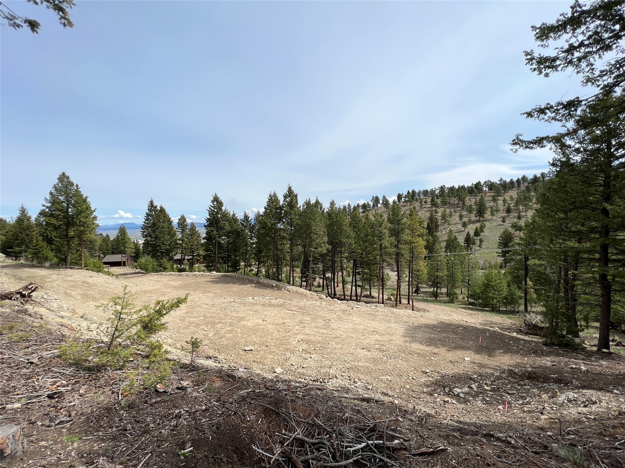 Cleared building site on a pine-covered hillside with distant mountain views and utility lines.