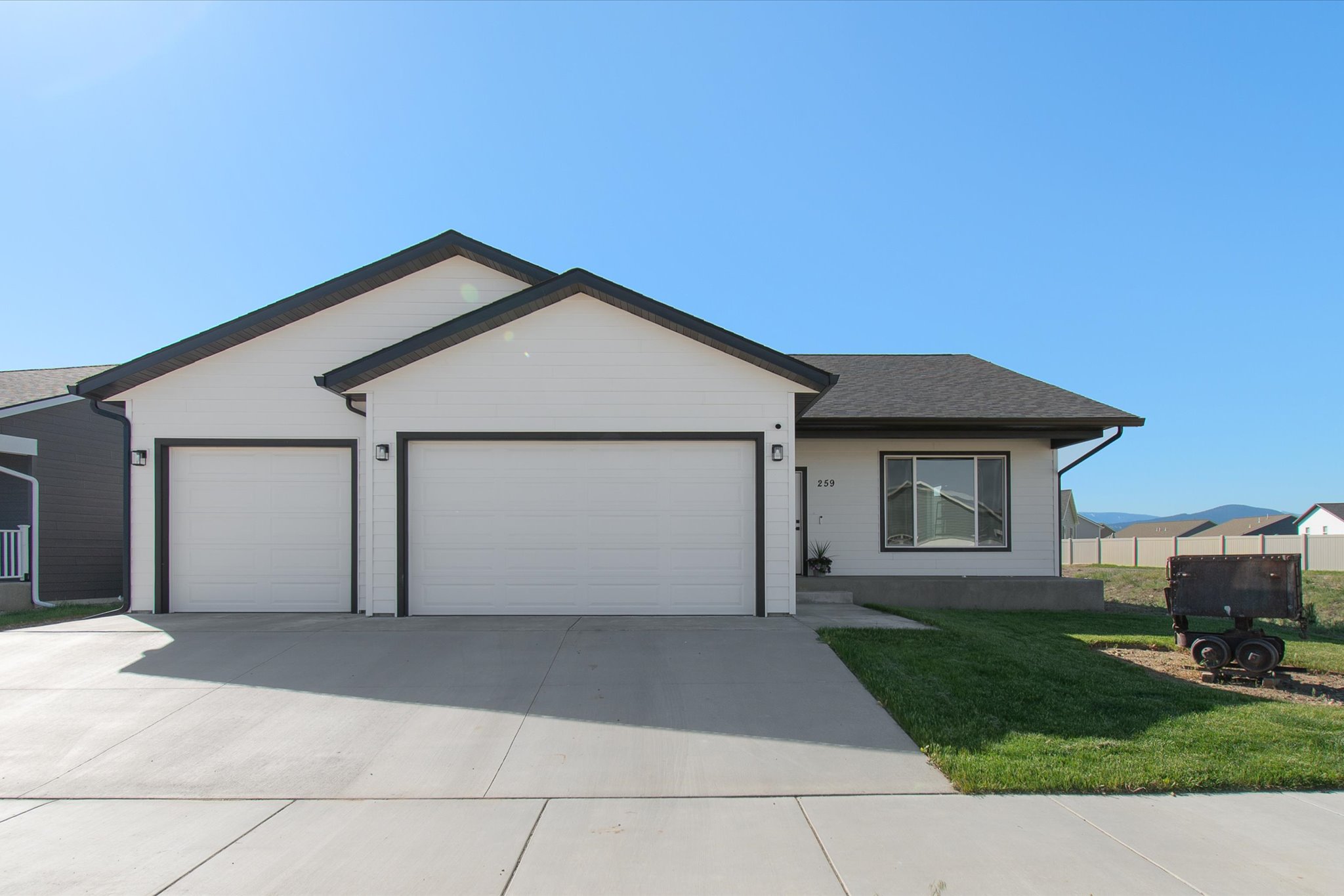 Single-story white house with two garage doors, dark trim, and a wide concrete driveway.