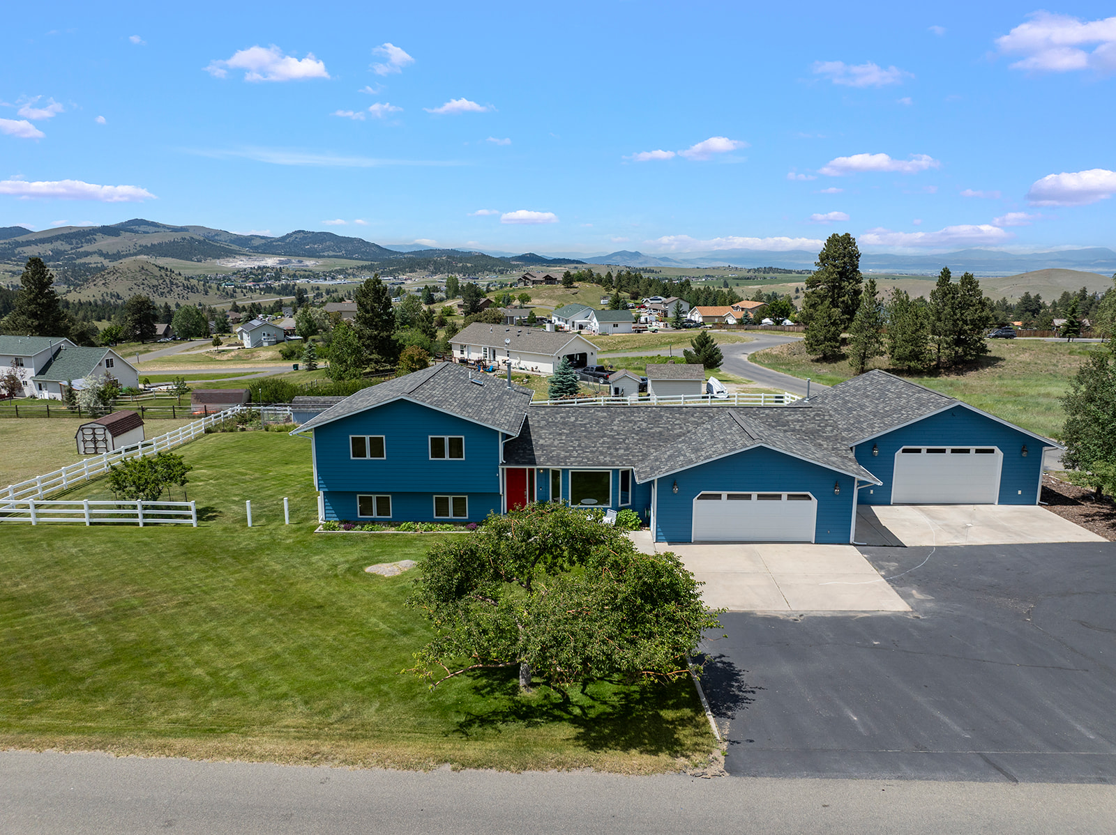Blue two-story house with two garage bays, a fenced lawn, and mountain views.