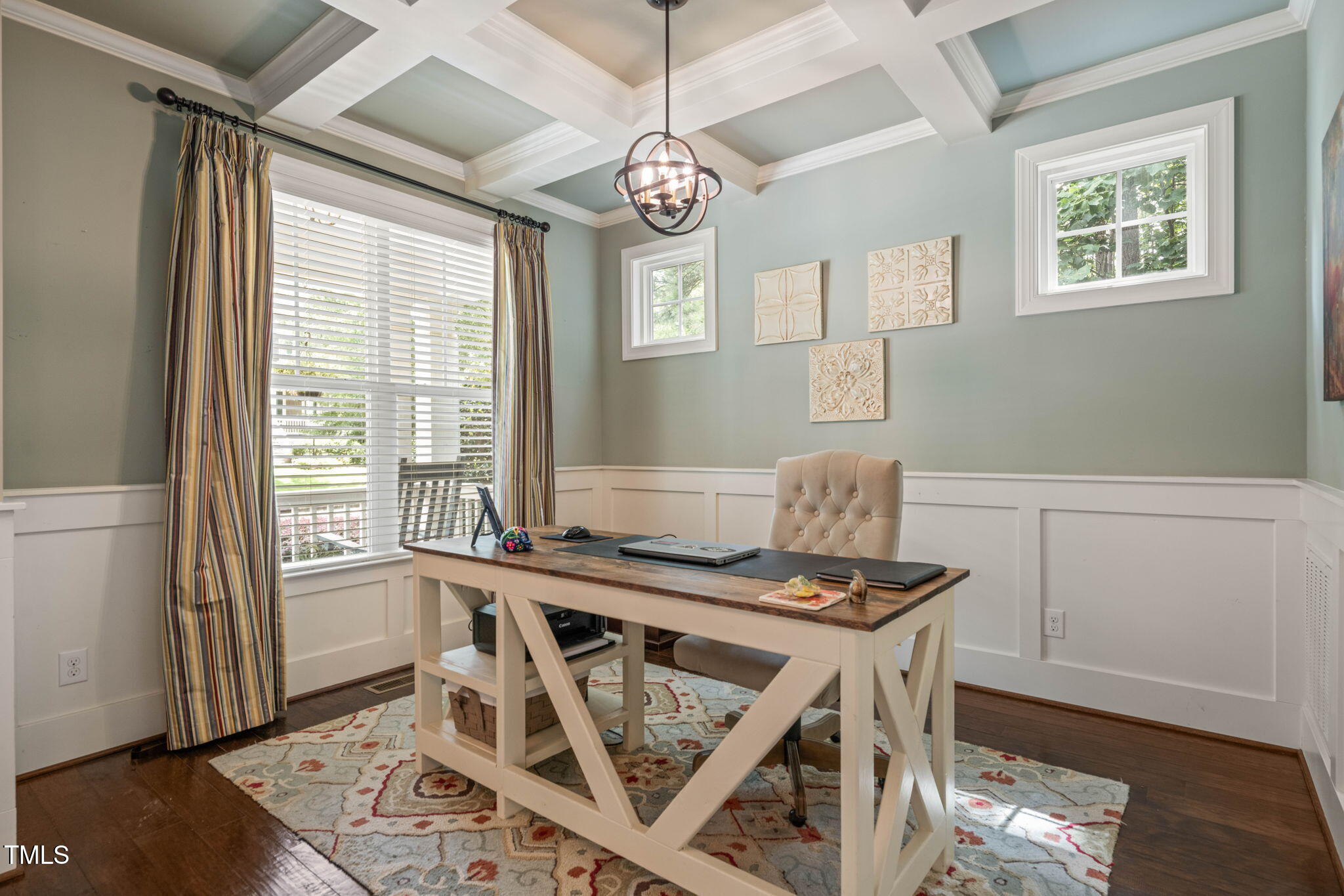 Furnished home office with a coffered ceiling, wood-top desk, and striped curtains beside a large window.