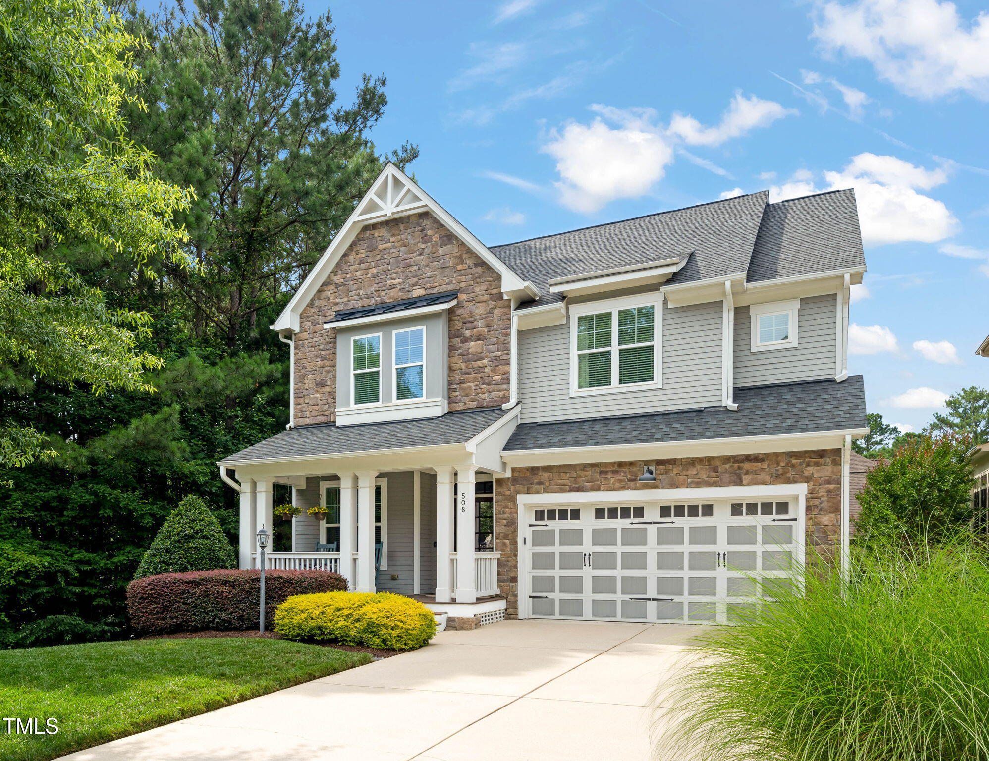 Two-story stone and gray-sided home with a covered porch, white double garage door, and landscaped front yard.