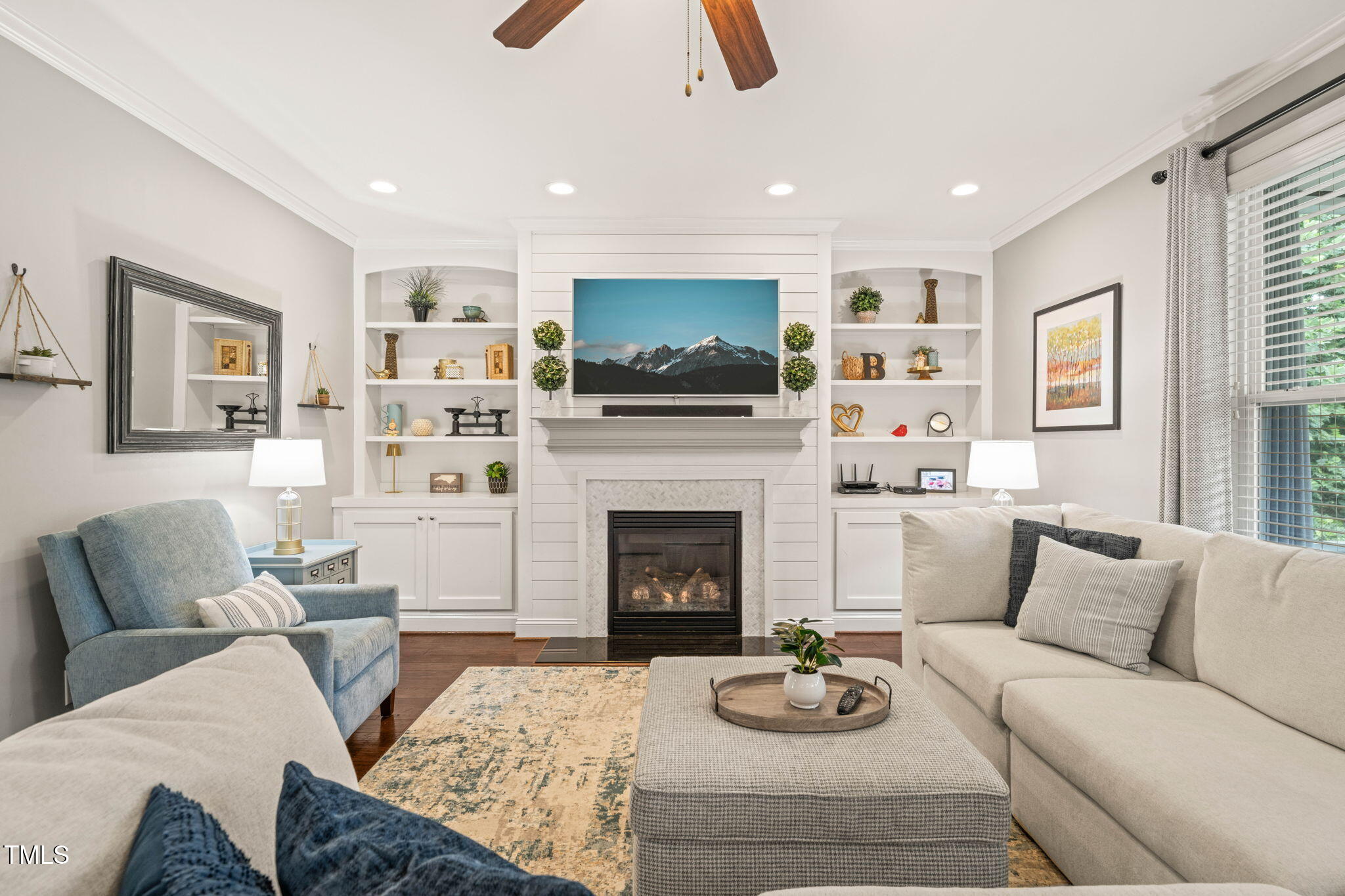 Living room with a white built-in fireplace, display shelves, and seating around an upholstered ottoman.