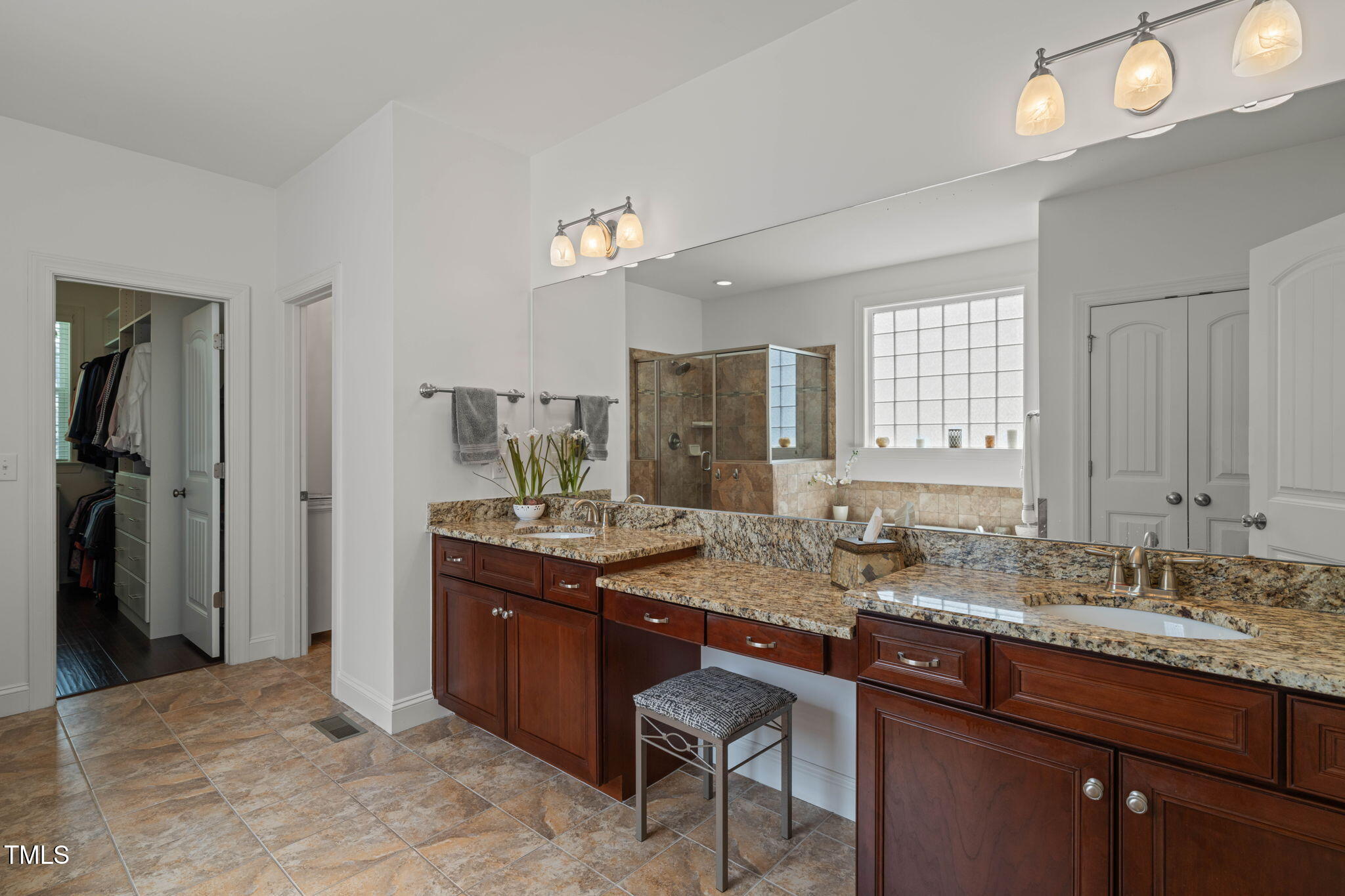 Primary bathroom with a long double vanity, granite countertops, and a tiled walk-in shower.