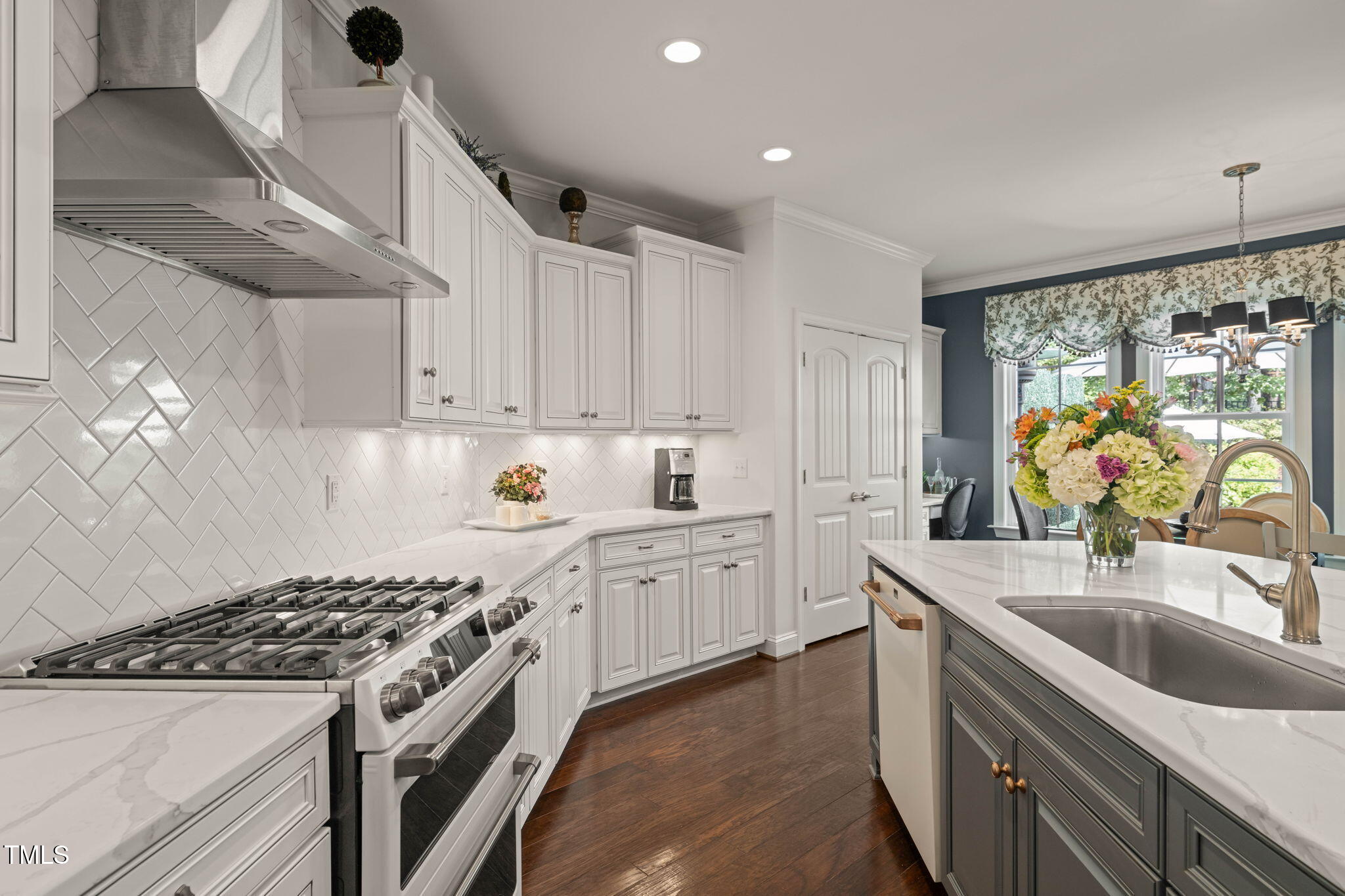 Kitchen with white cabinets, a stainless steel range, herringbone tile backsplash, and a large sink island.