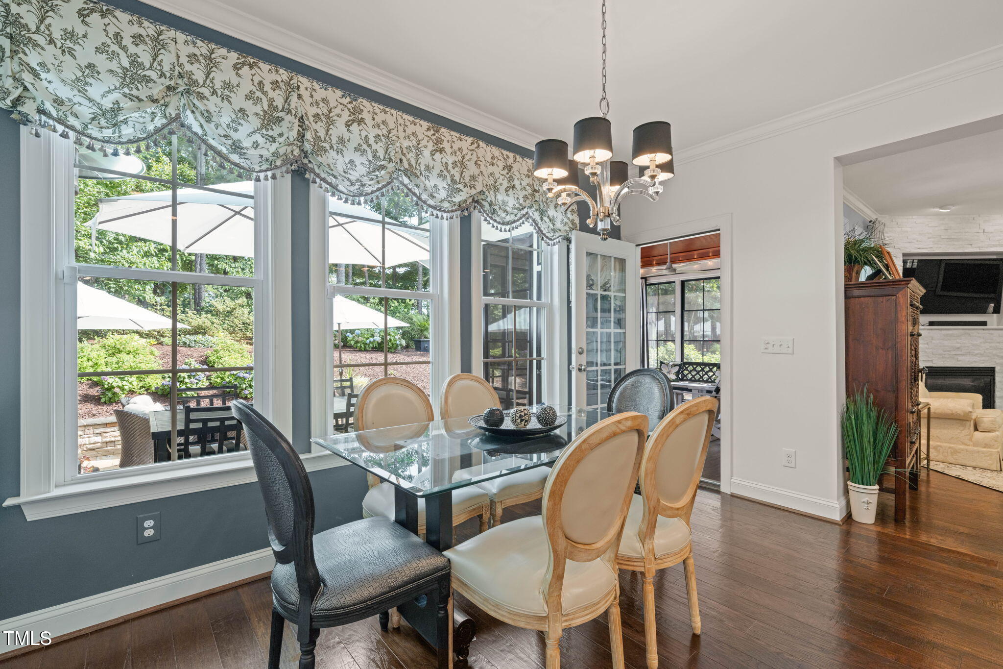 Dining room with a glass-top table, patterned window valance, and leafy patio view.