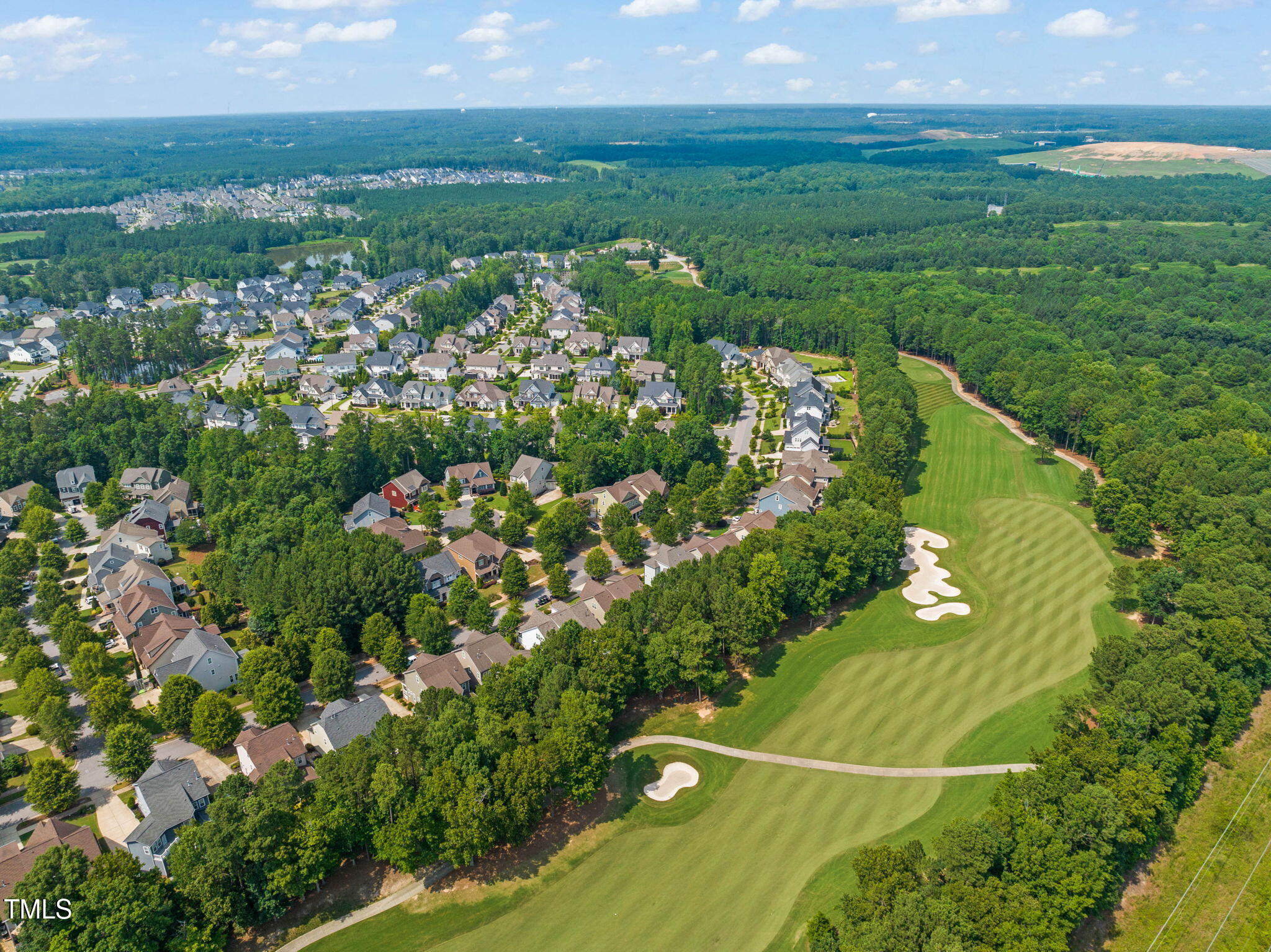 Aerial view of homes bordering a golf course with striped fairways and sand bunkers.