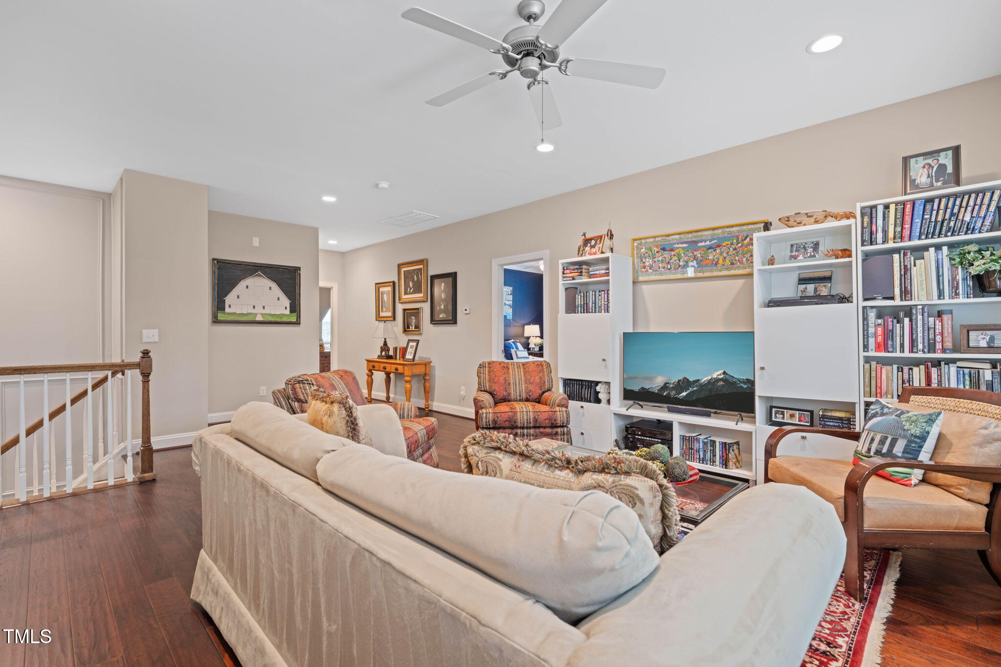 Furnished living room with hardwood floors, a ceiling fan, and white bookshelves around the television.