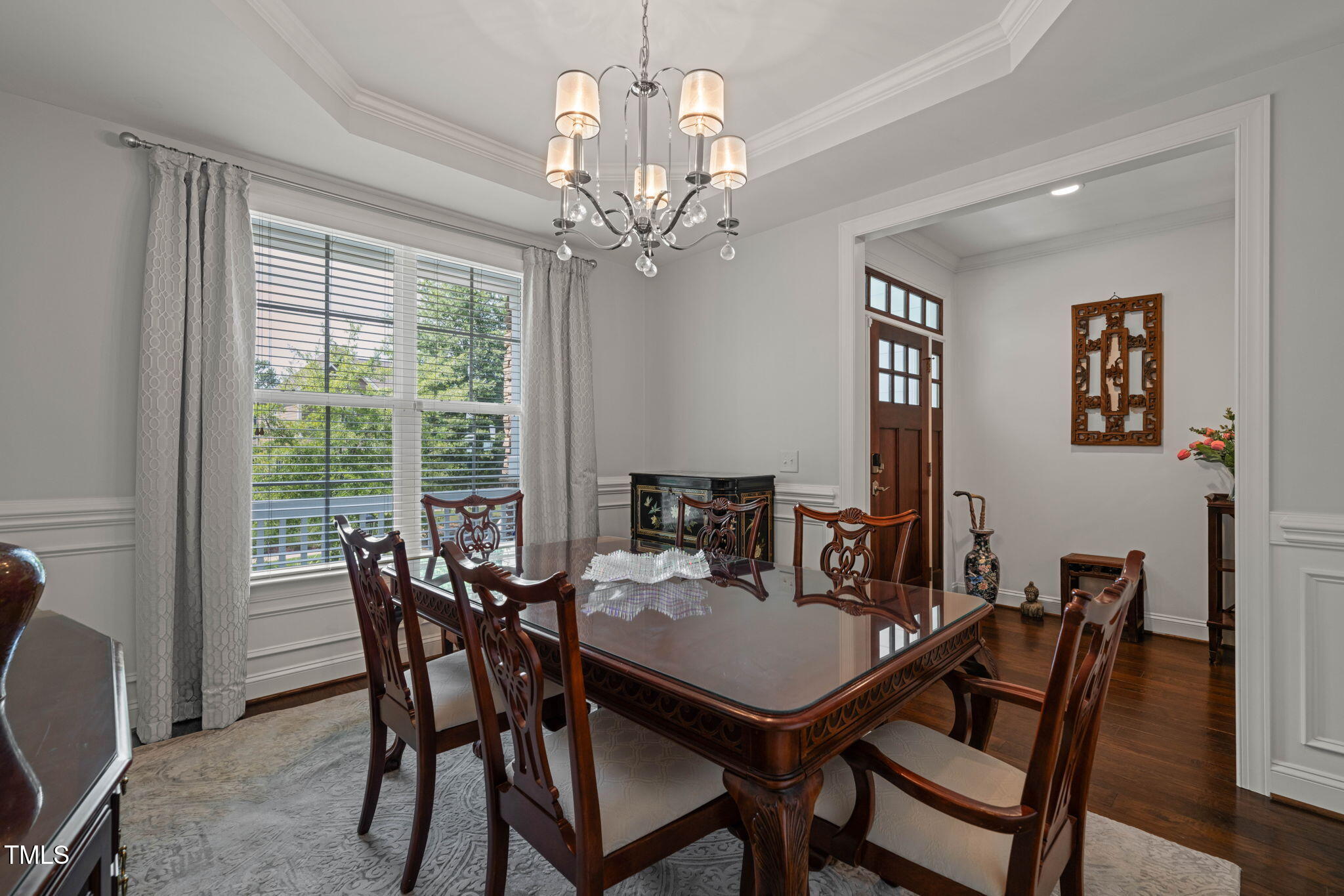 Dining room with a carved dark wood table, chandelier, and large curtained windows.