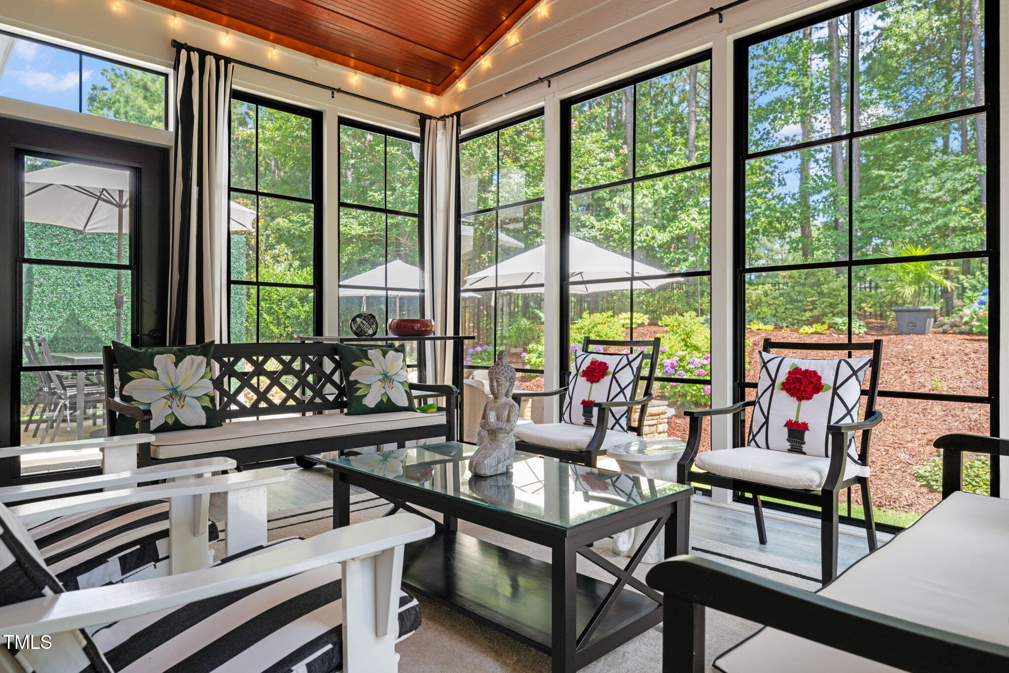 Sunroom with tall garden-facing windows, floral cushions, and a glass coffee table.