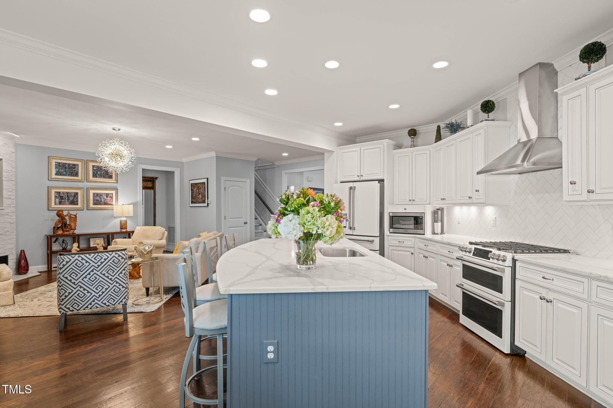 Open kitchen with white cabinetry, stainless steel appliances, and a large blue island beside the living area.