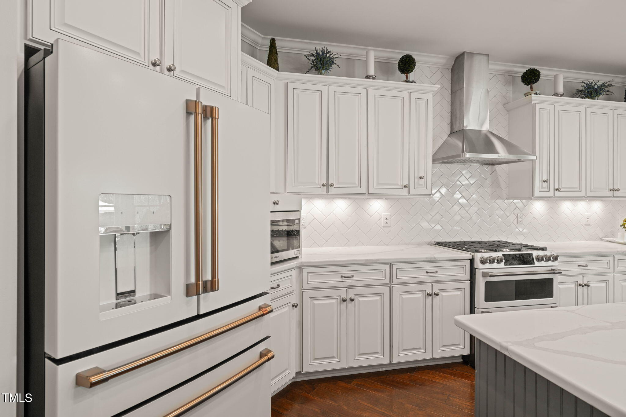 Kitchen with white cabinetry, herringbone tile backsplash, stainless steel range, and brass-handled refrigerator.