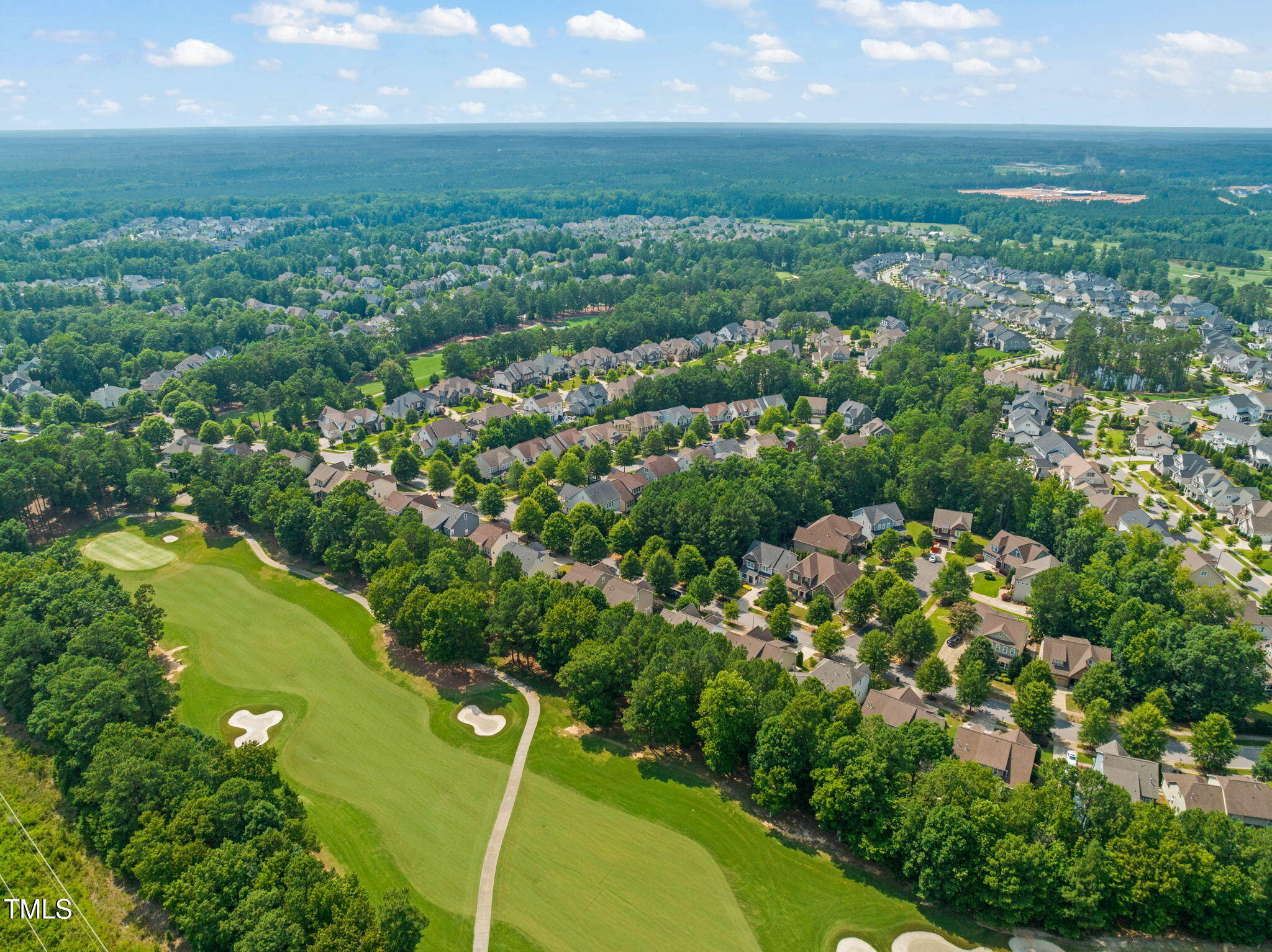 Aerial view of a tree-lined neighborhood beside a golf course with fairways and sand bunkers.