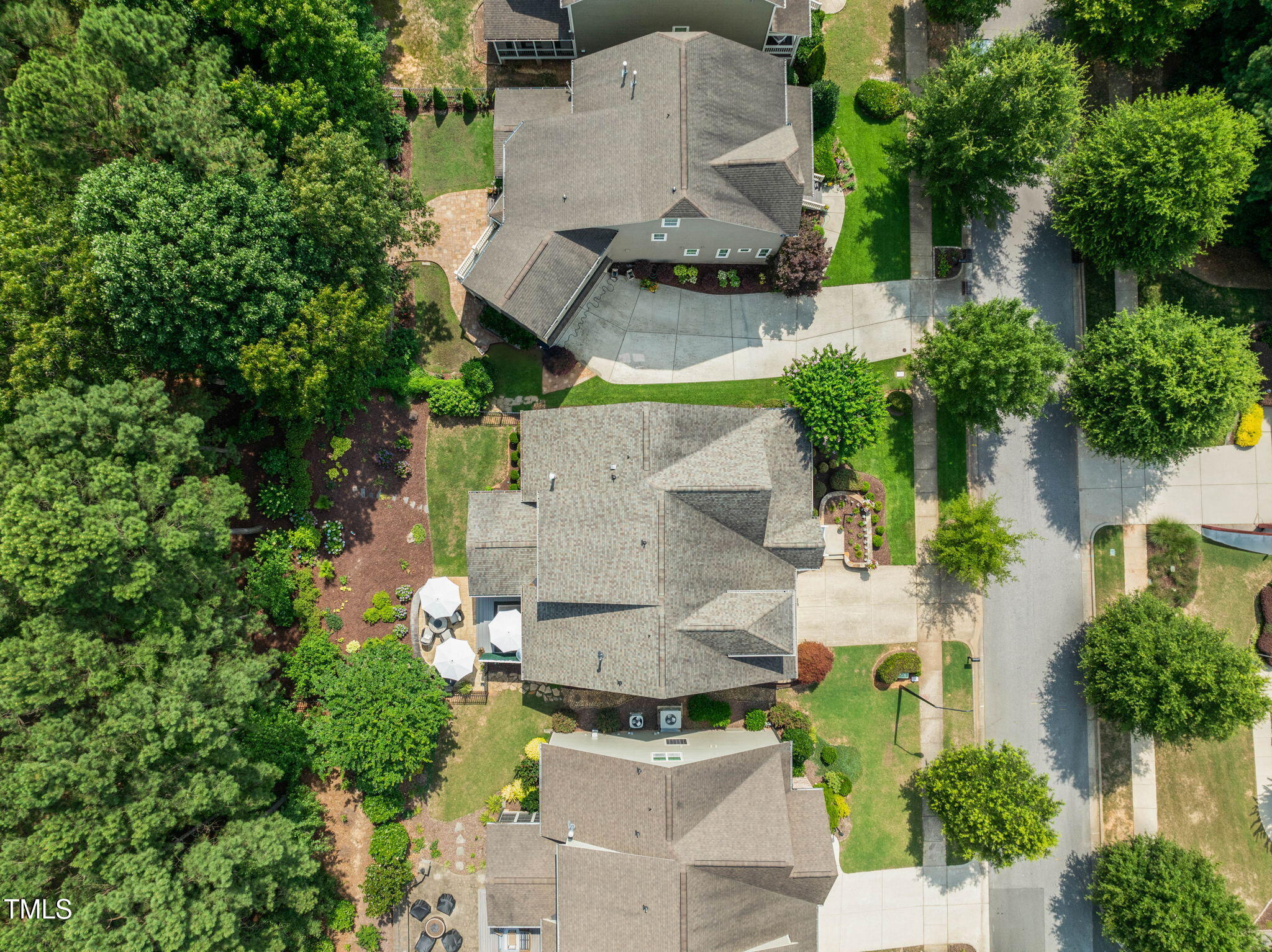 Aerial view of a home with a broad driveway, landscaped yard, and mature trees.