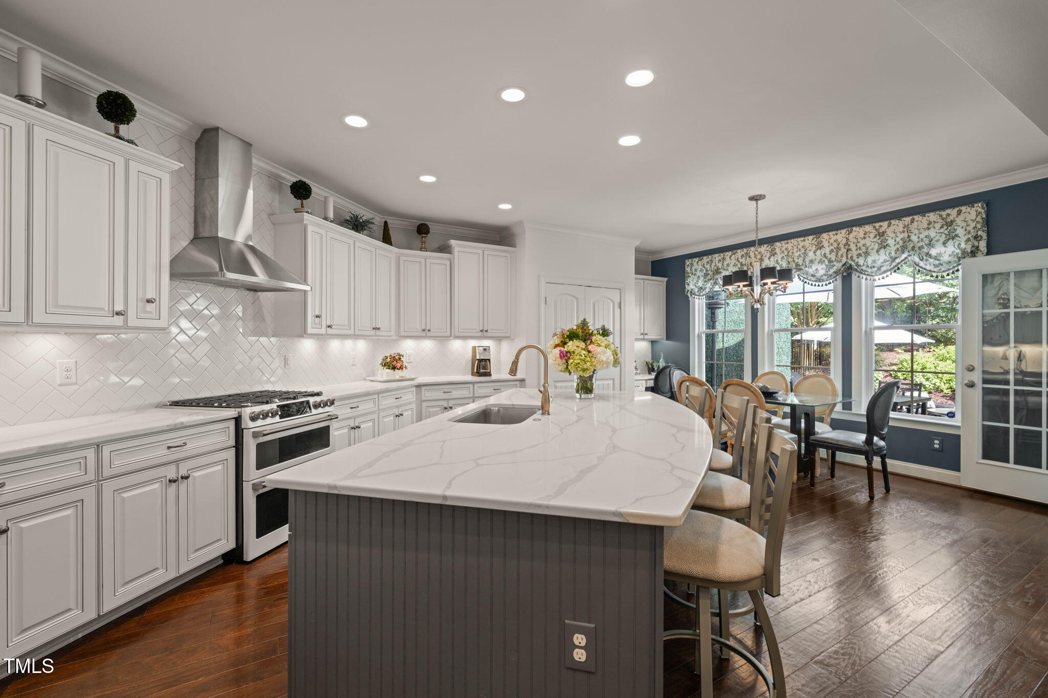 Kitchen with a large veined-stone island, white cabinetry, stainless range, and adjoining dining area.