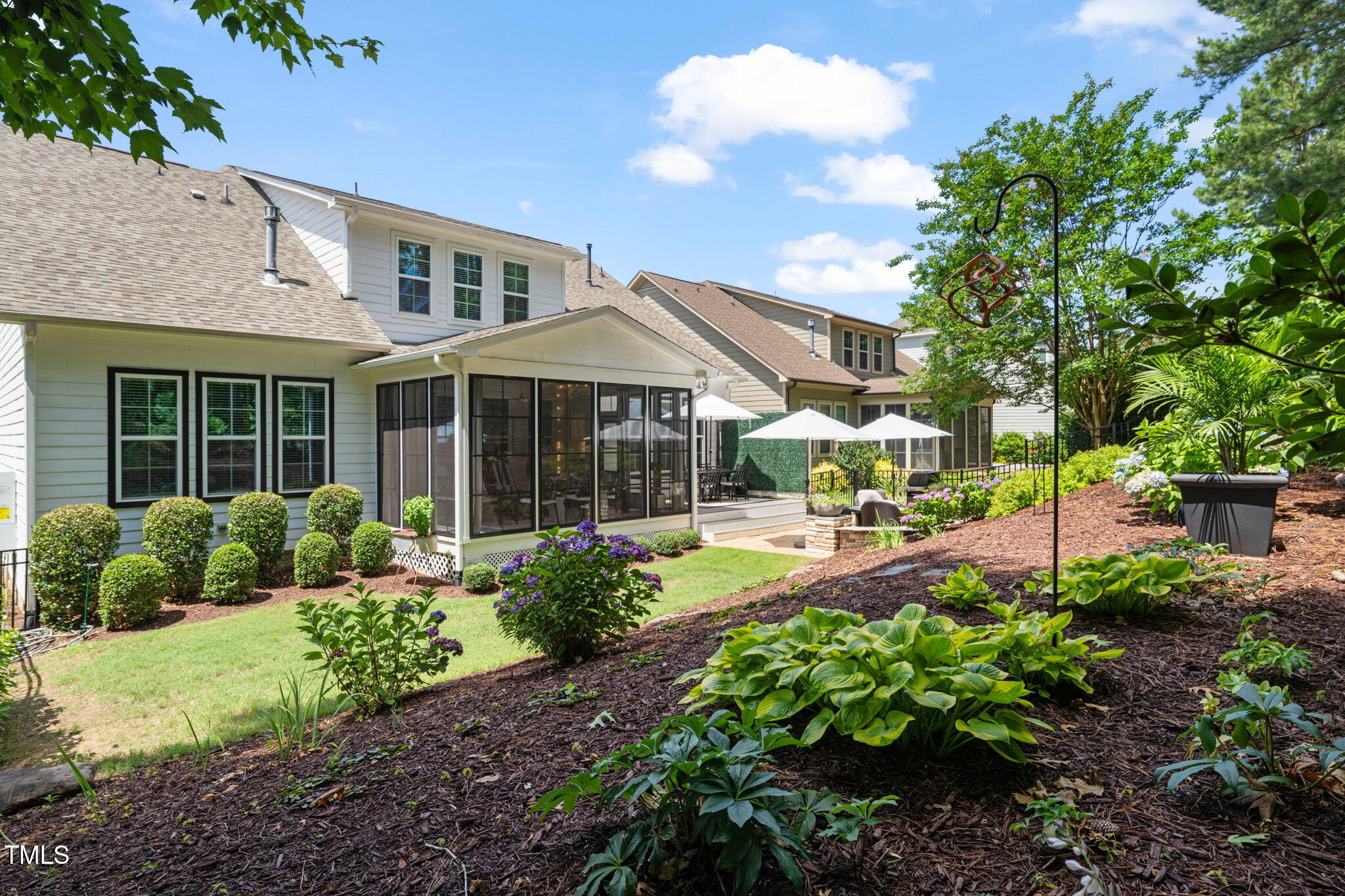 Rear exterior of a two-story home with a screened porch, patio umbrellas, and landscaped garden.