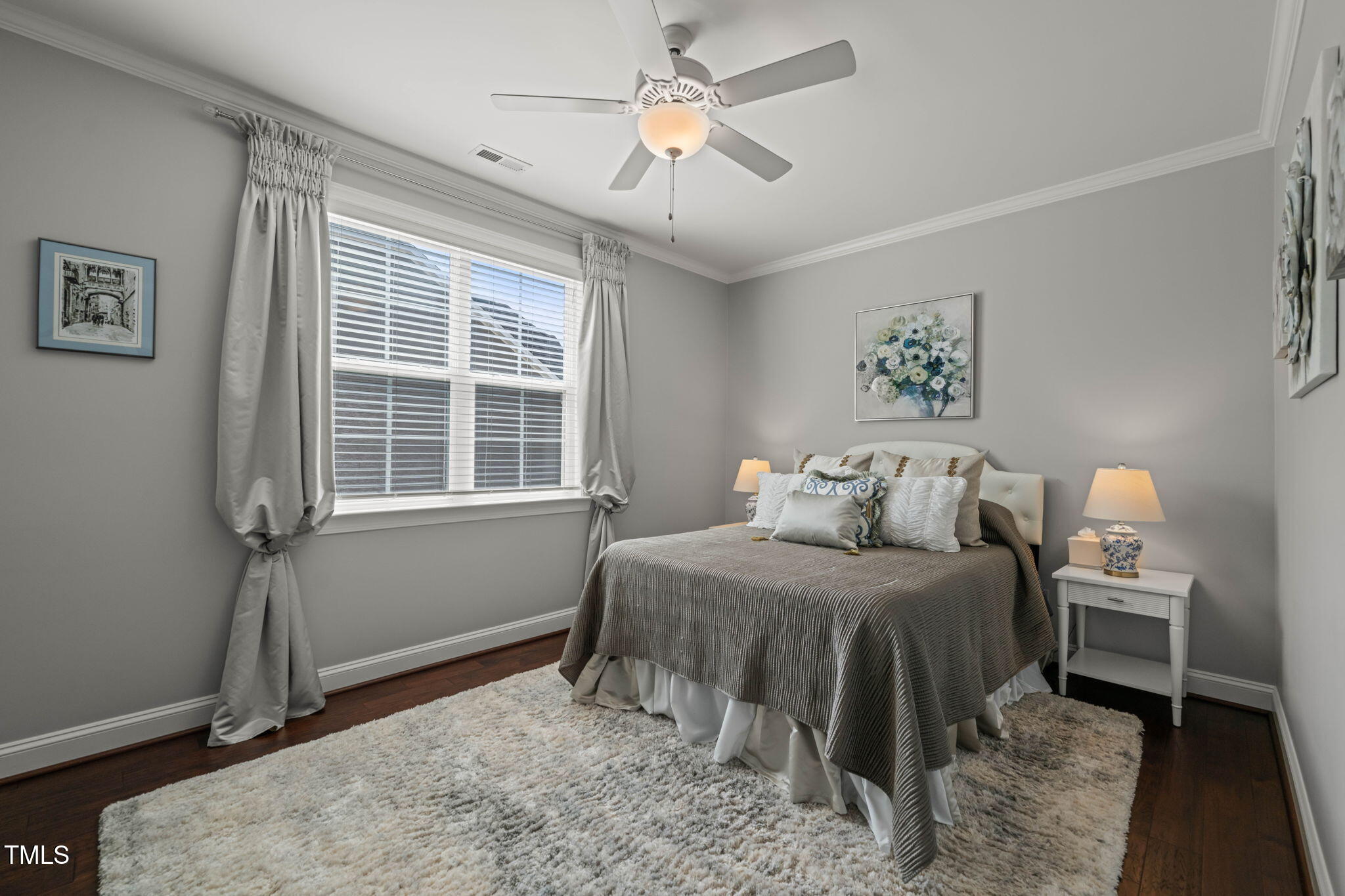 Furnished bedroom with a gray bed, large curtained window, dark wood floors, and a light shag rug.