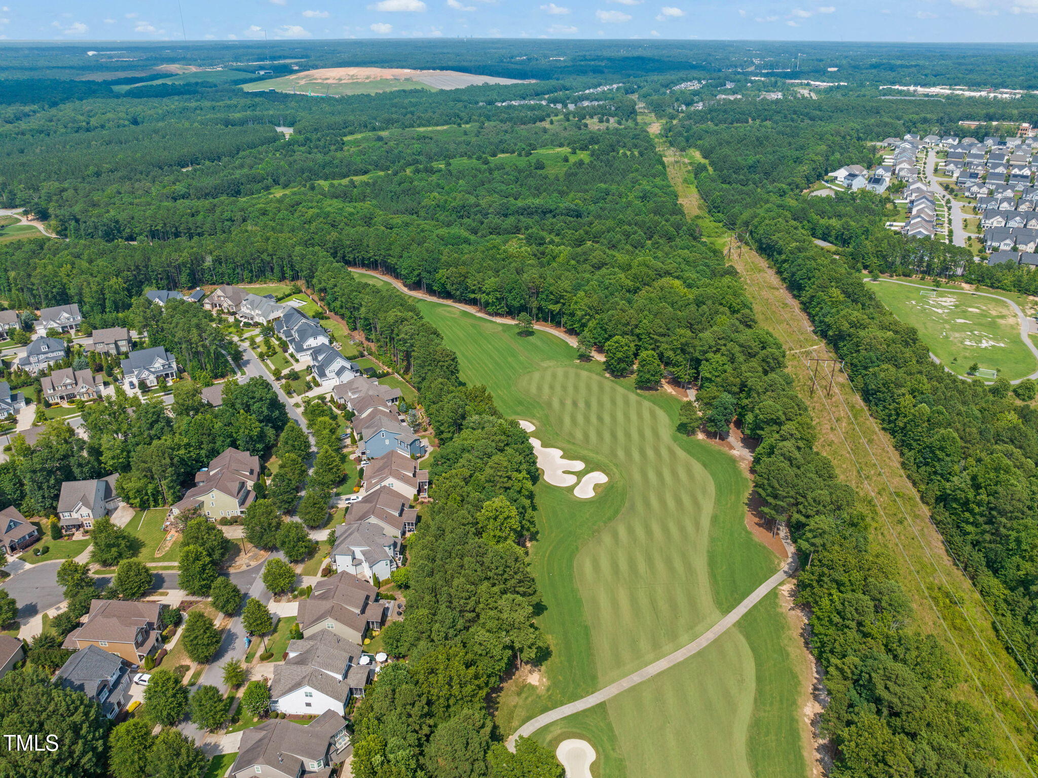Aerial view of a golf course beside homes, with tree-lined fairways and white sand bunkers.