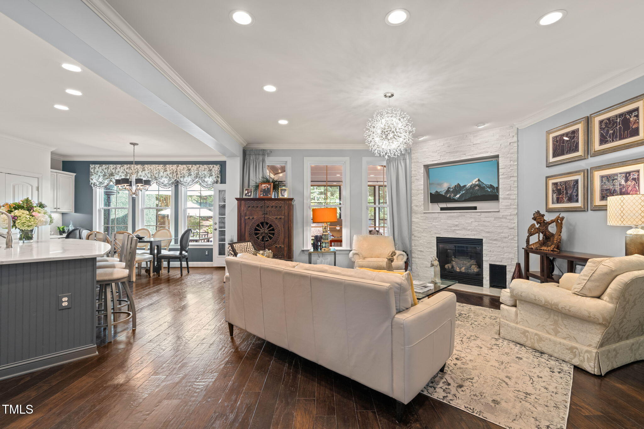 Open-plan living room with stone fireplace, cream sofas, dark hardwood floors, and adjoining kitchen and dining area.