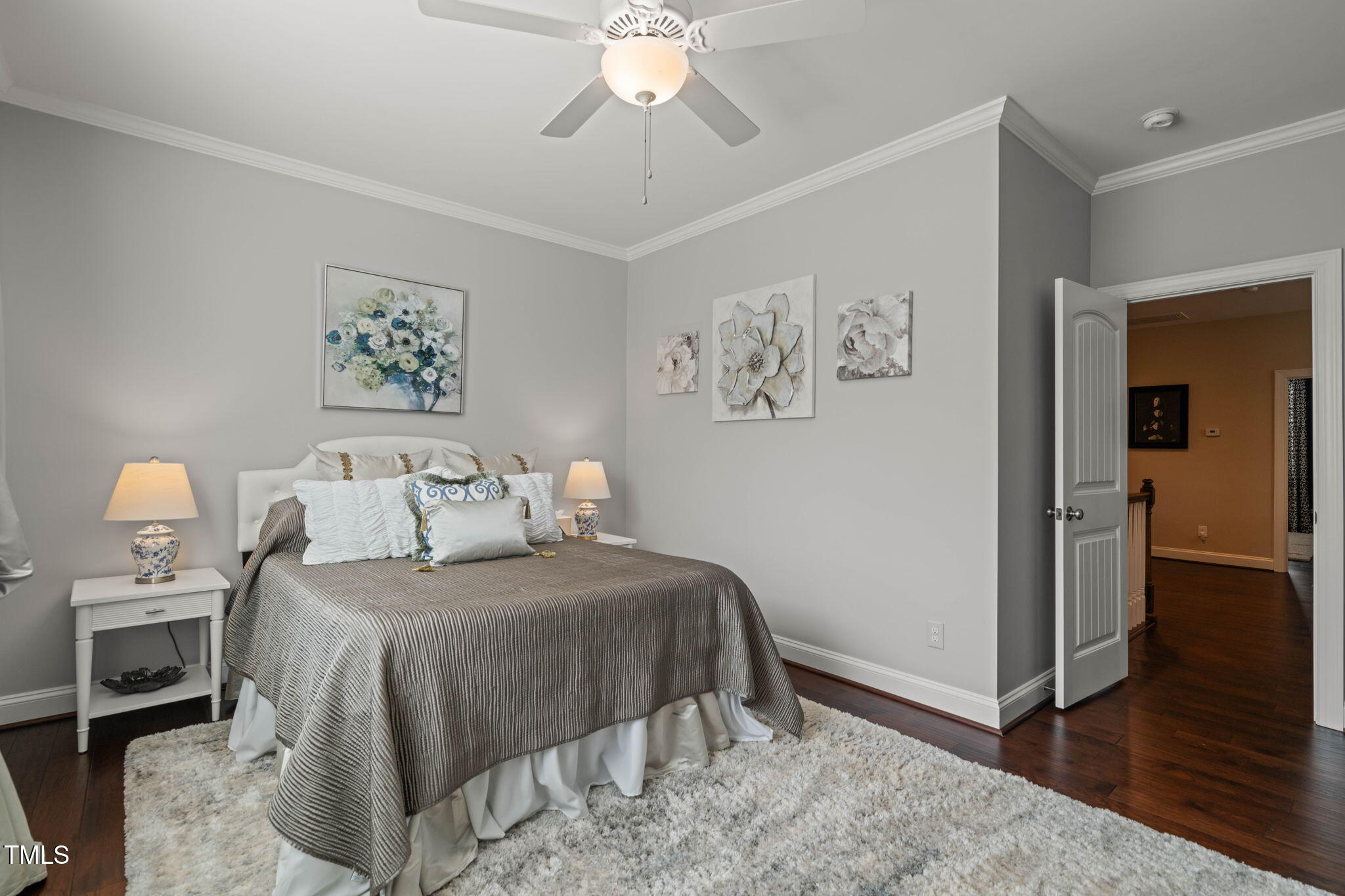 Bedroom with a gray bed, floral wall art, dark hardwood floors, and an open door to the hallway.