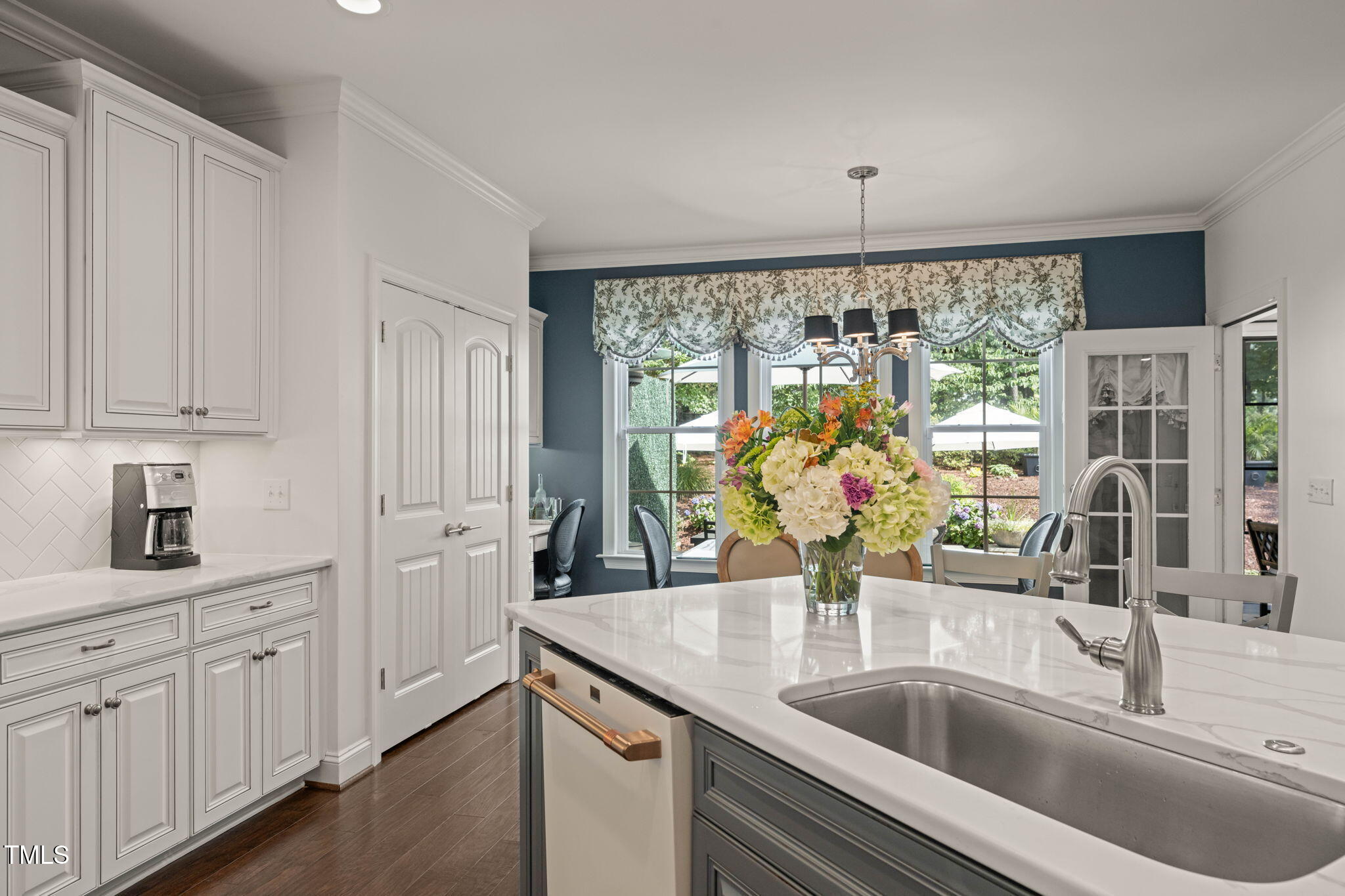 Kitchen with white paneled cabinets, a large island sink, and garden-facing windows with floral valances.