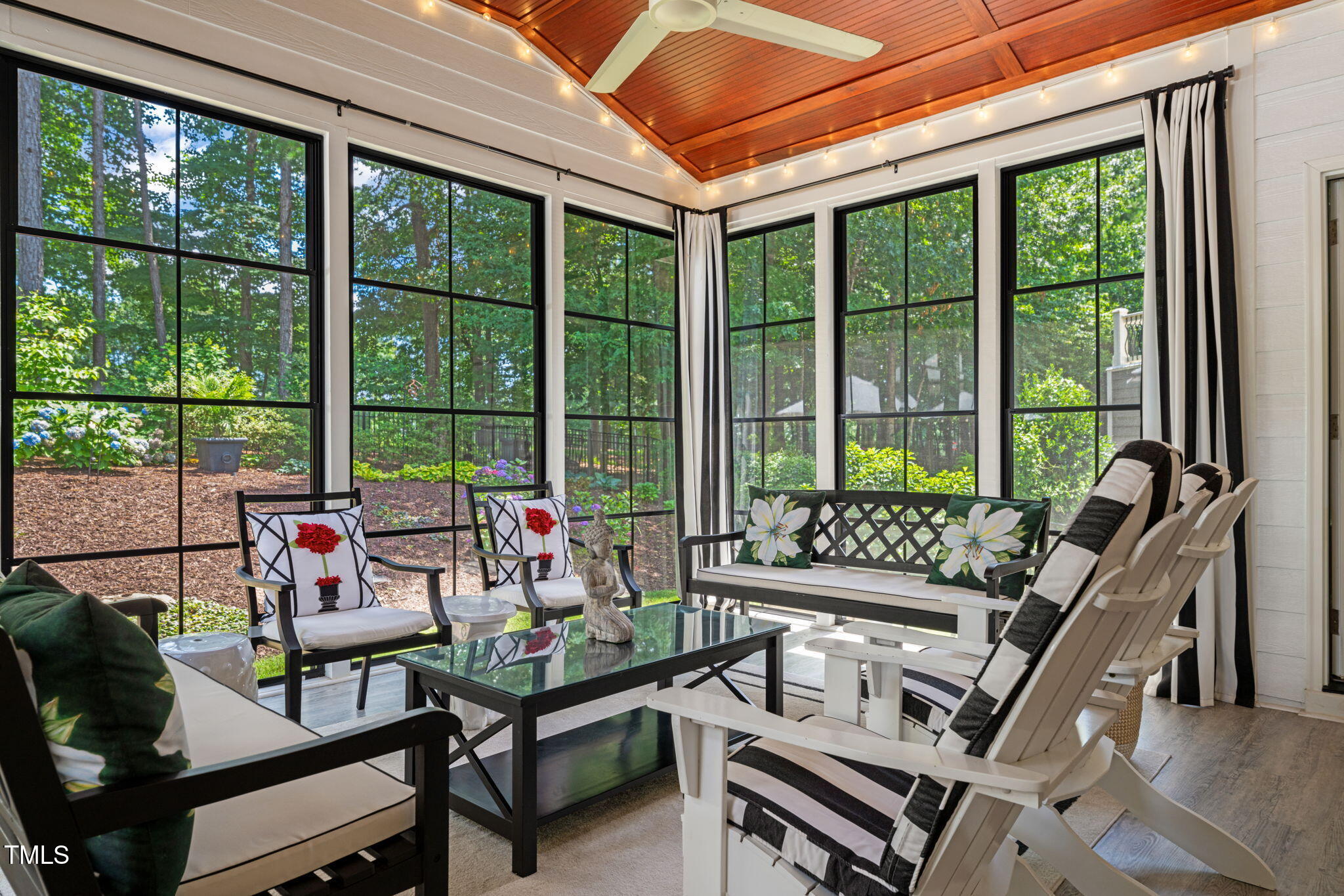 Furnished sunroom with expansive garden-facing windows and a vaulted wood ceiling.