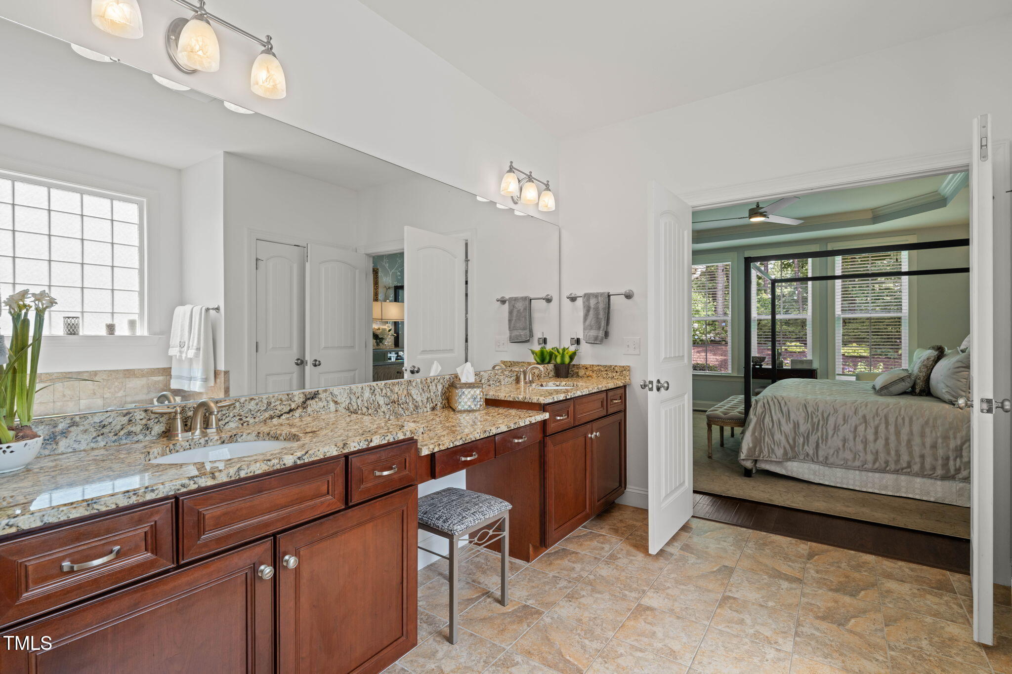 Bathroom with a granite double vanity and dark wood cabinets, opening into a bedroom.