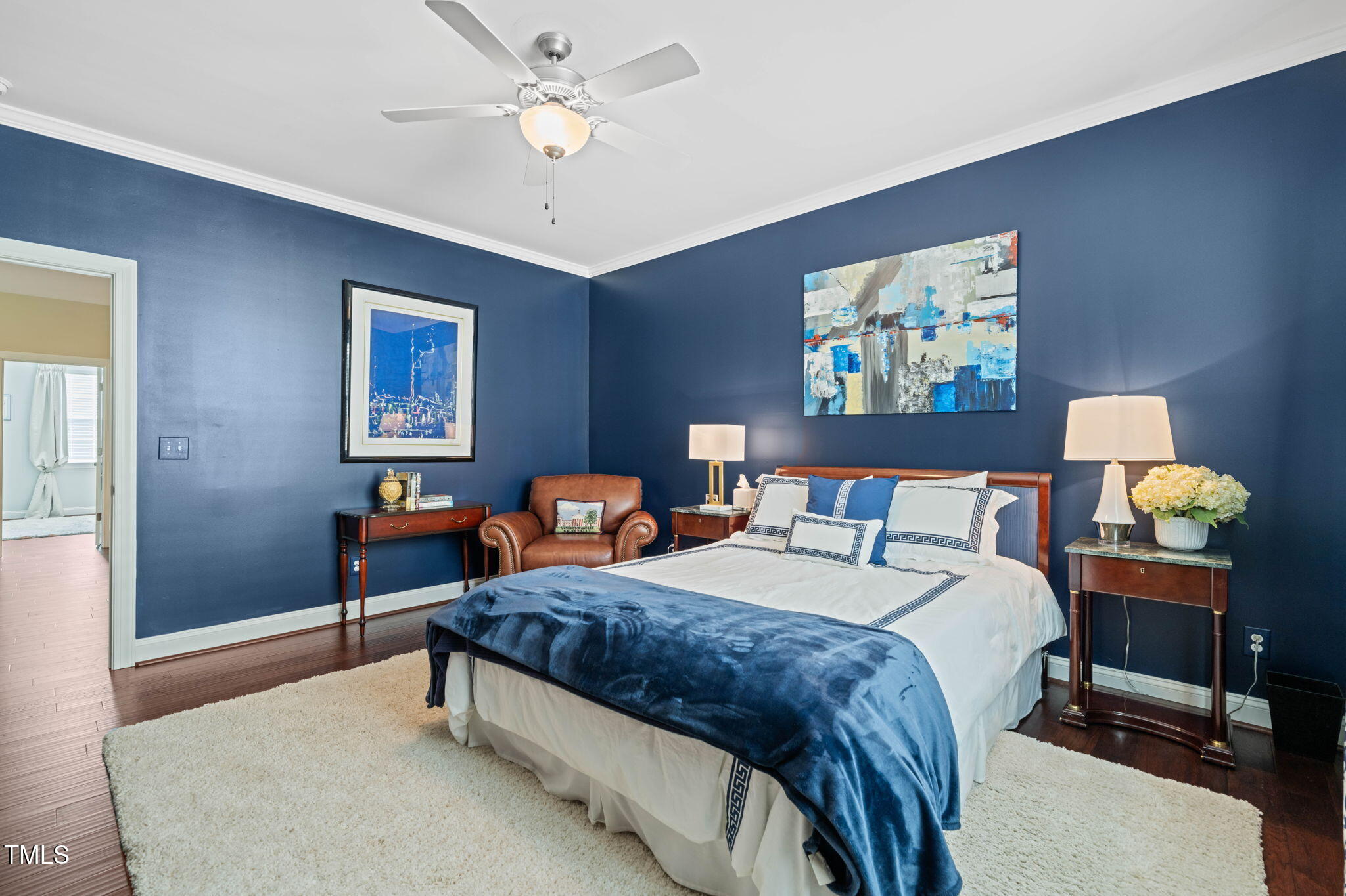 Staged bedroom with deep blue walls, a white bed and blue throw, and a brown leather armchair.