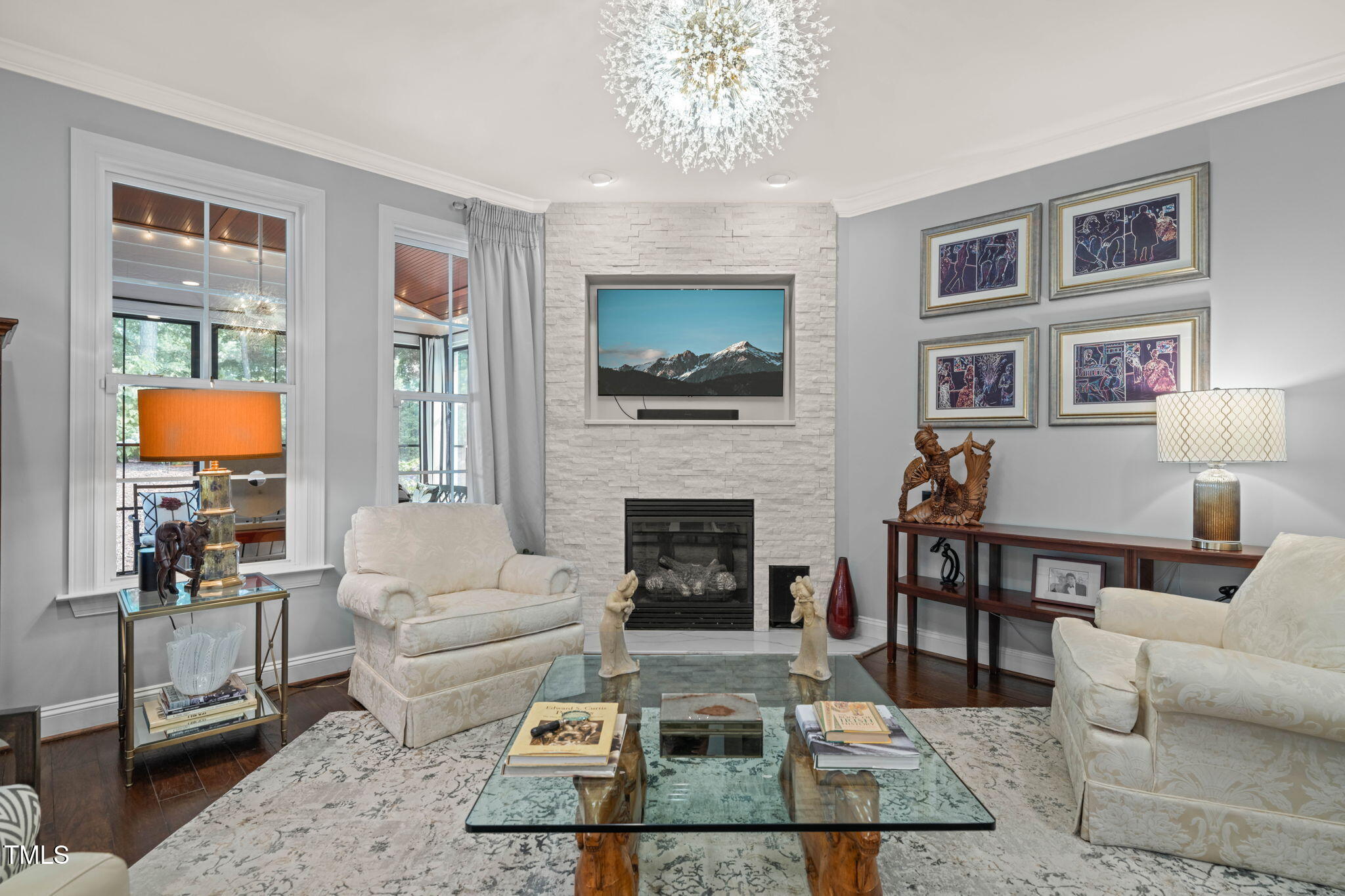 Living room with a white stone fireplace, cream seating, glass coffee table, and large windows.