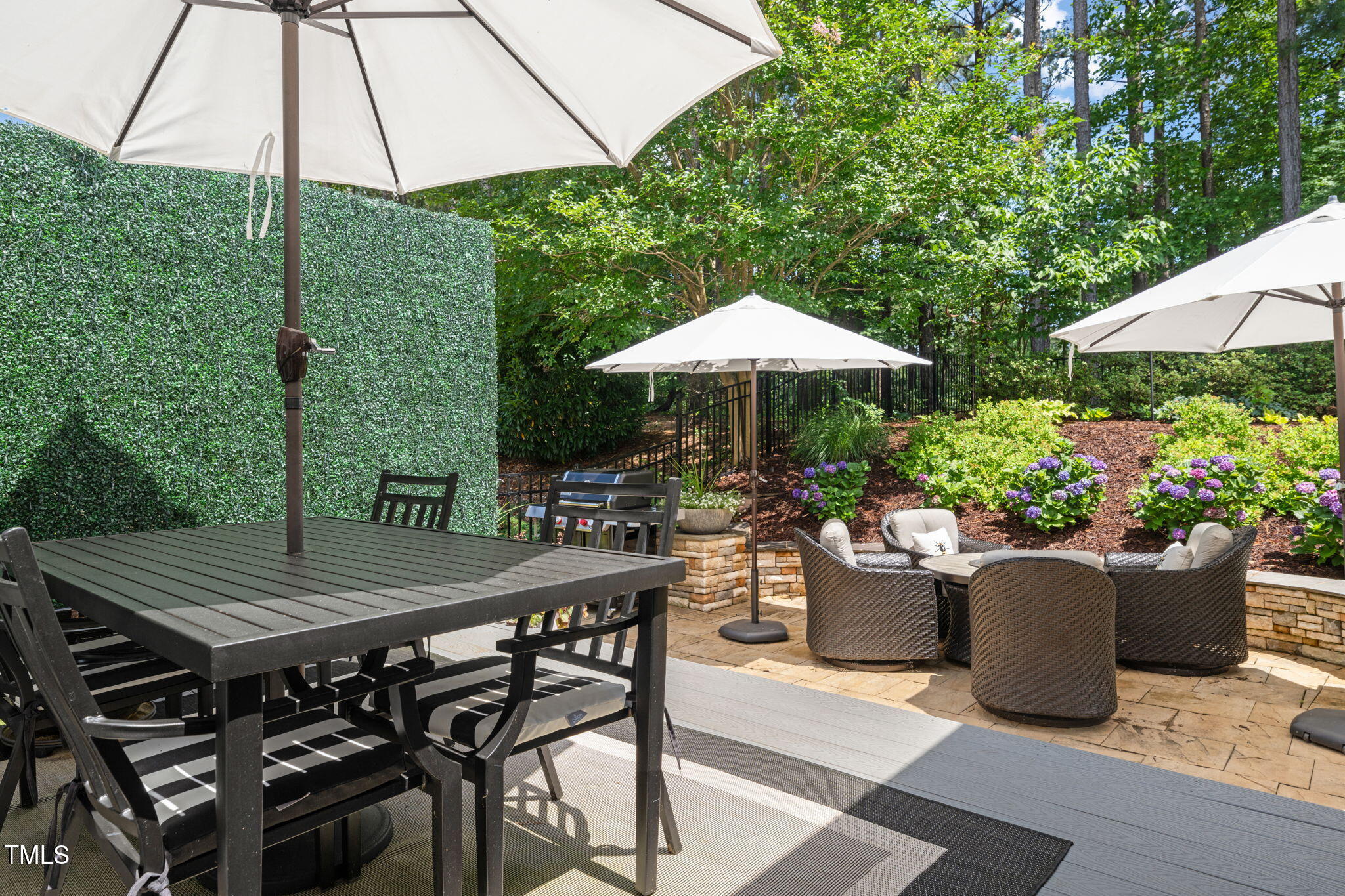 Outdoor patio with umbrella-shaded dining table, wicker seating, and flowering hydrangeas.