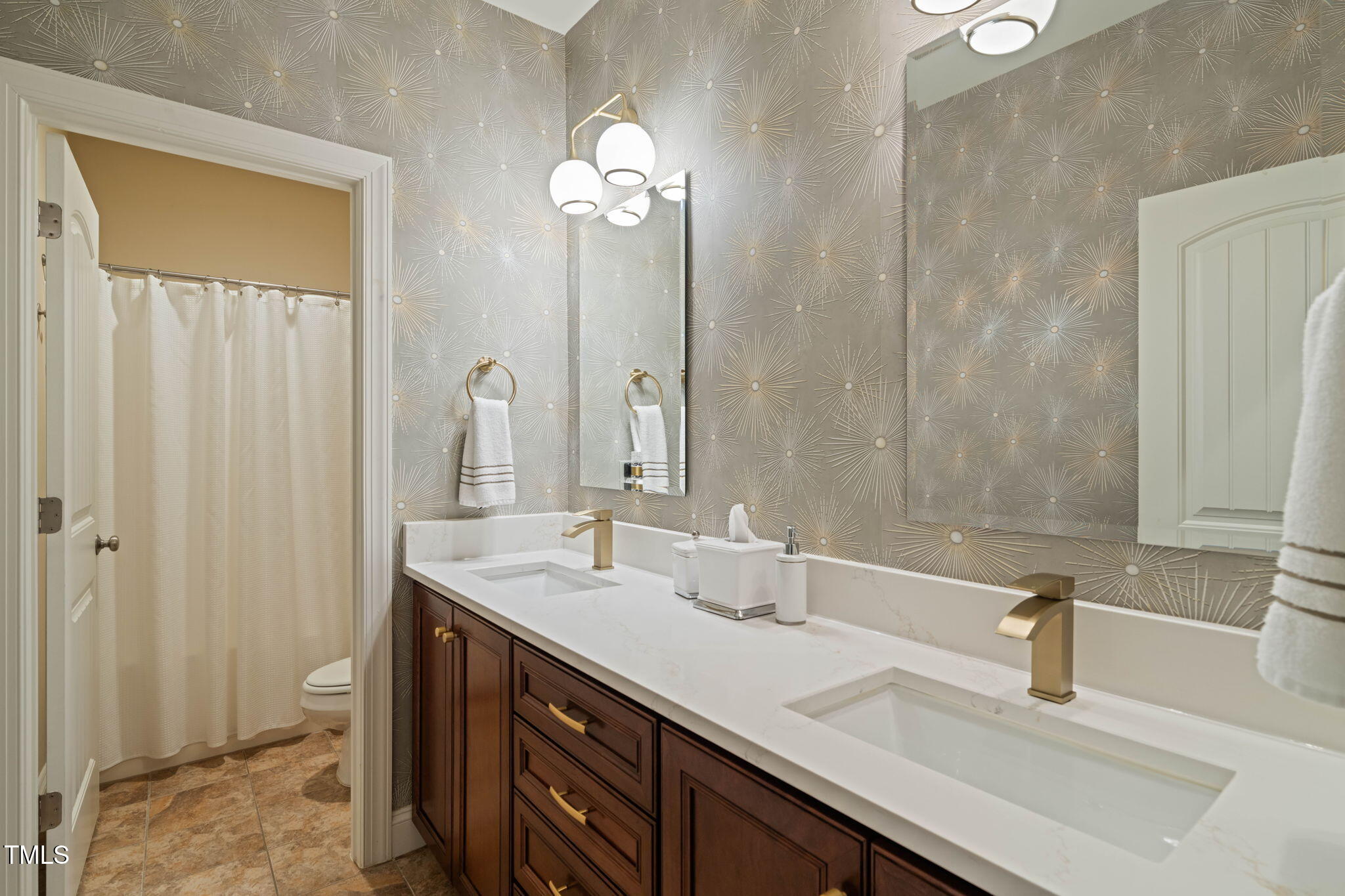Bathroom with a dark wood double vanity, brass faucets, and starburst-patterned wallpaper.