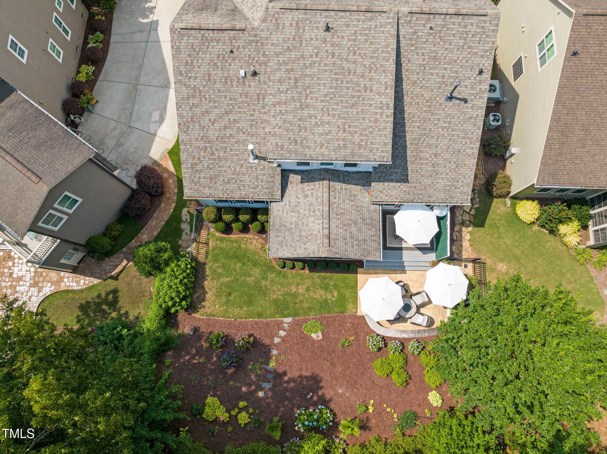 Aerial view of a home’s landscaped backyard with two patio areas shaded by white umbrellas.