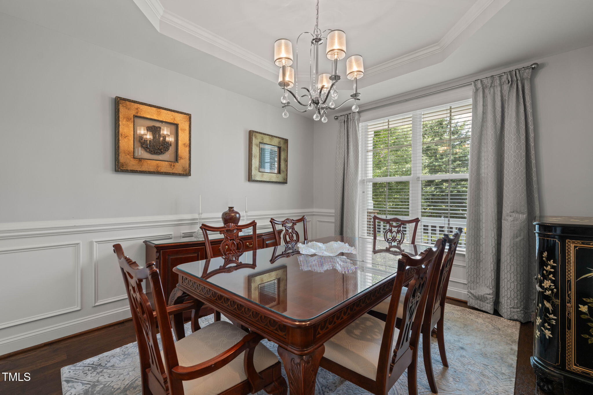 Formal dining room with carved dark wood furniture, chandelier, and large curtained window.