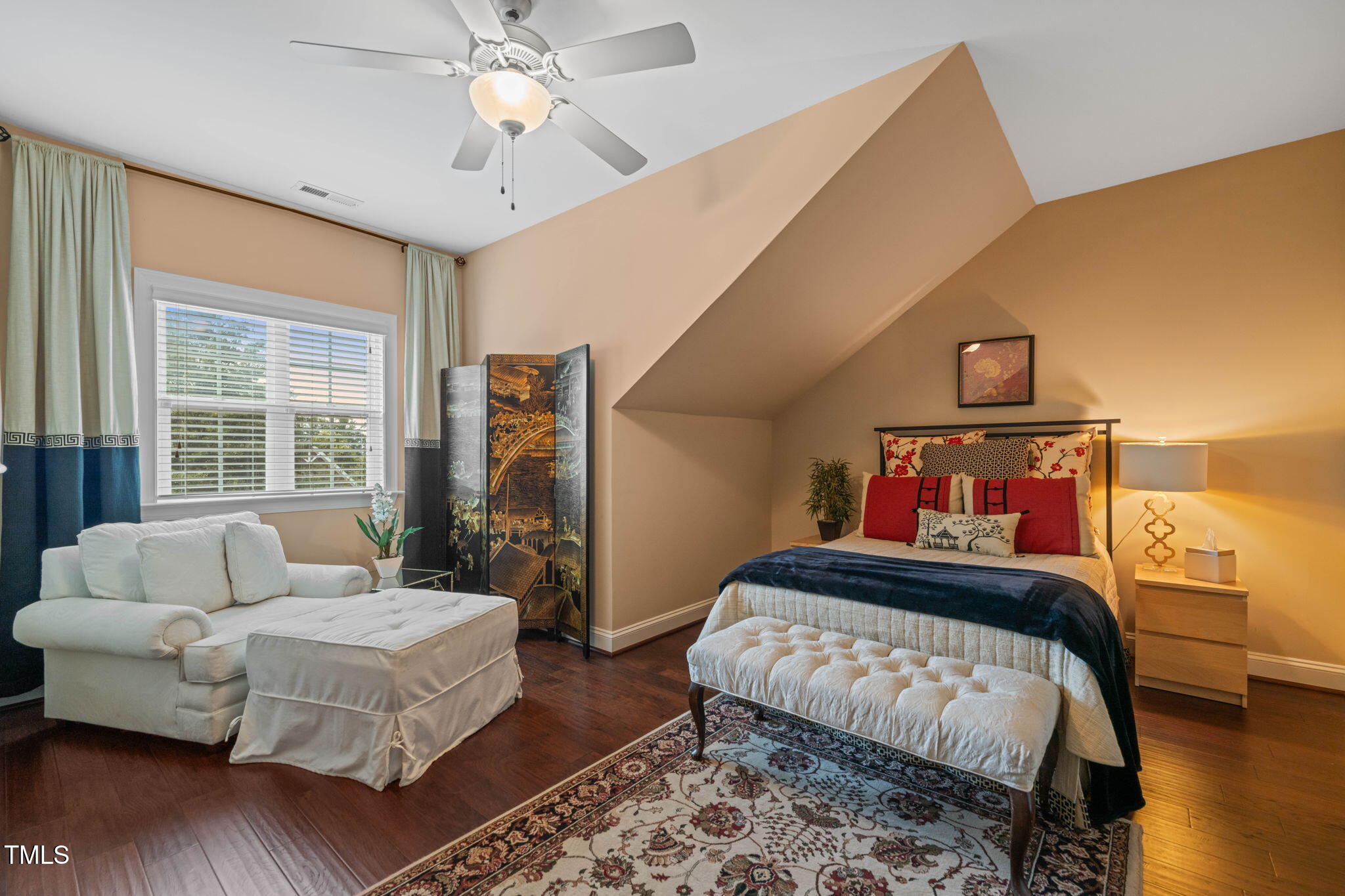 Furnished bedroom with a sloped ceiling, large bed, white chaise, and dark wood floors.