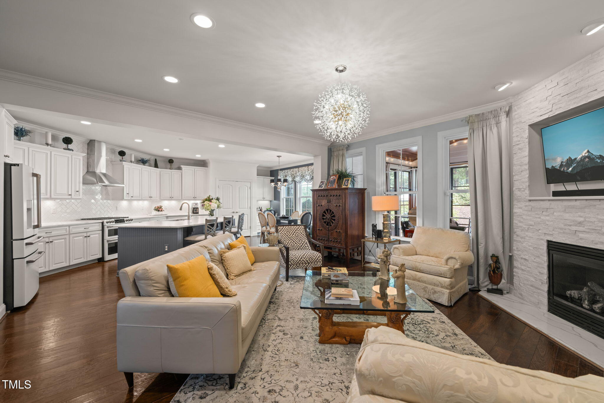 Open-plan living room and kitchen with white cabinetry, hardwood floors, and a stone fireplace.