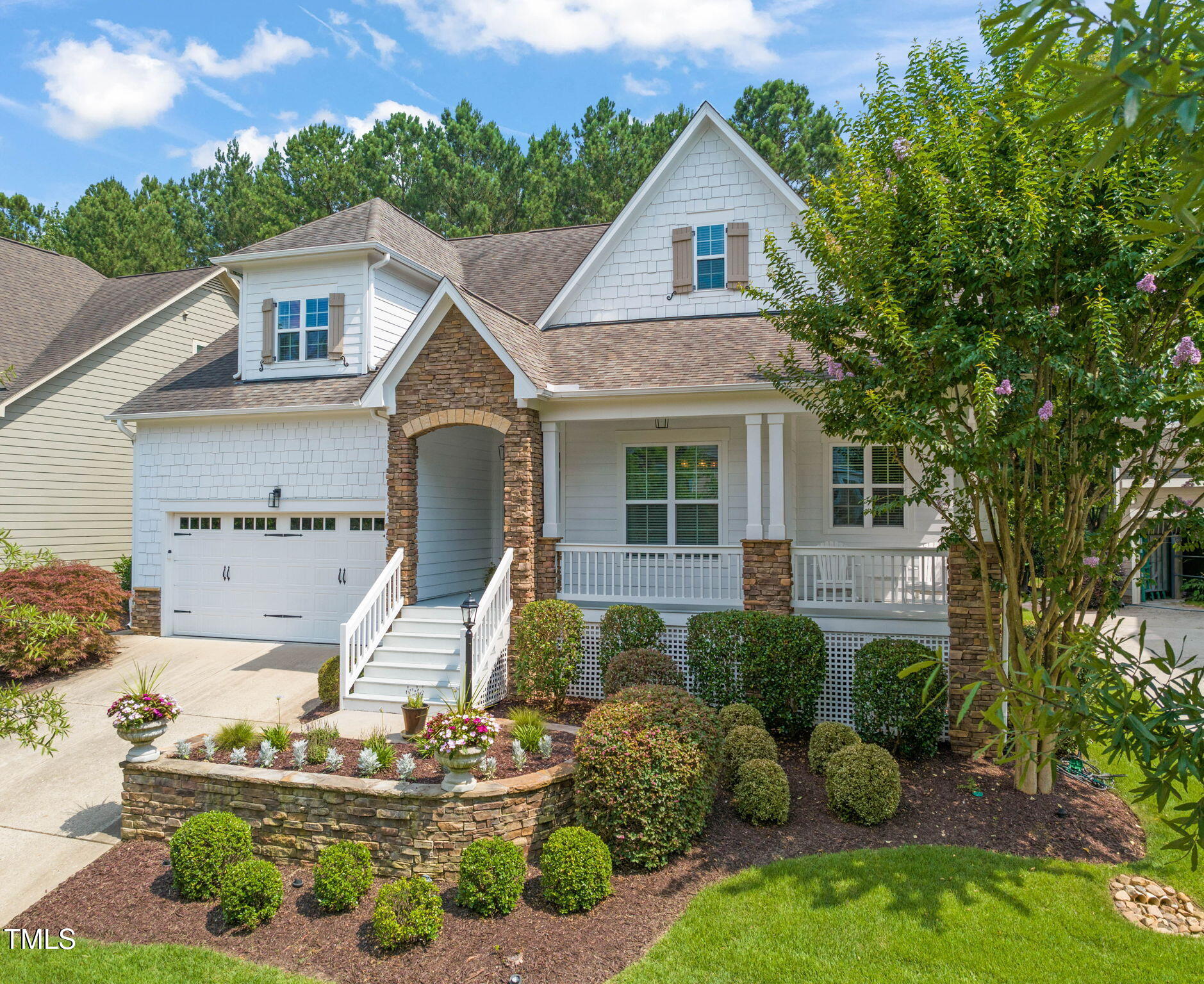White two-story home with stone-trimmed porch, attached garage, and landscaped front garden.