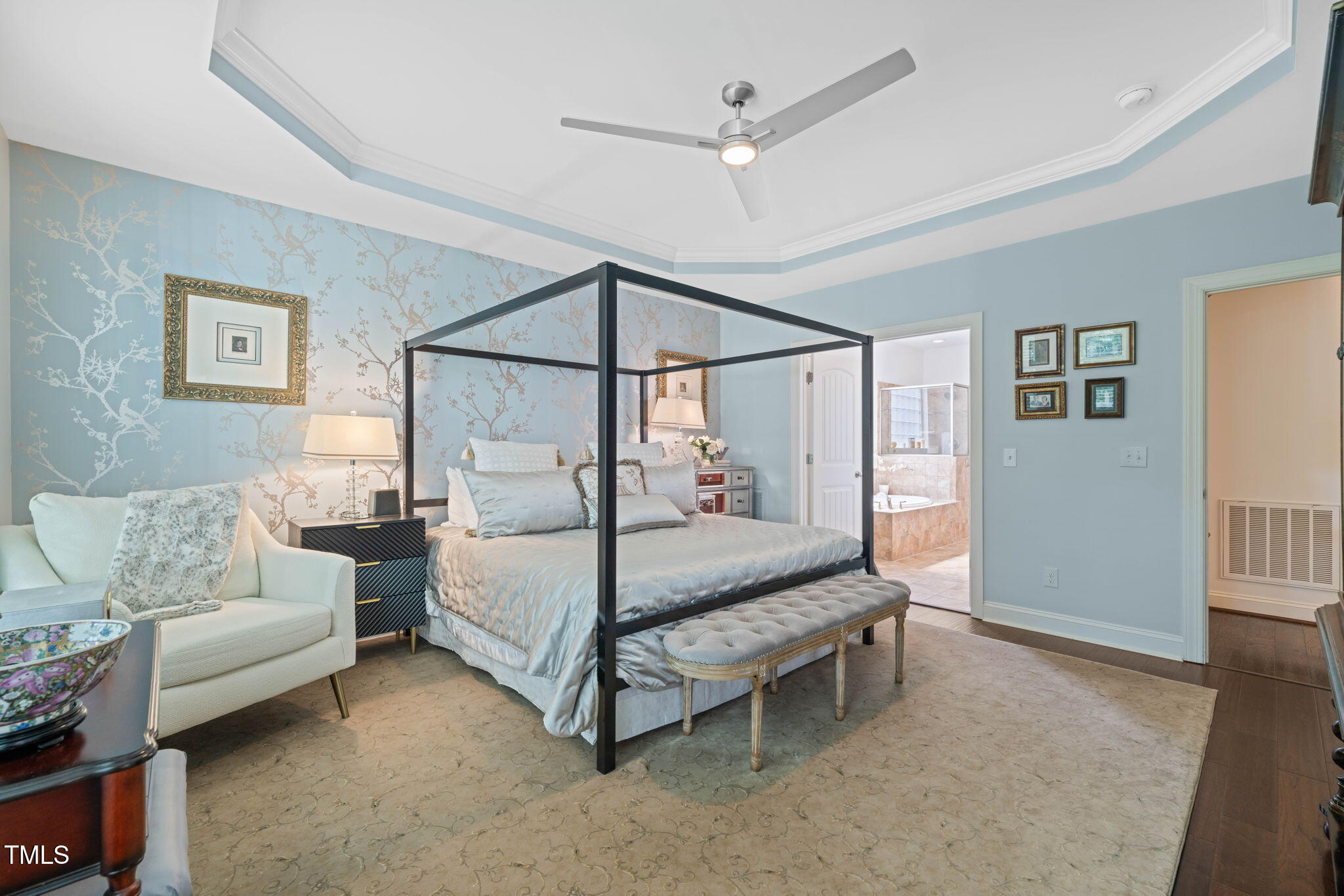 Primary bedroom with a black four-poster bed, pale blue patterned walls, and an open ensuite doorway.