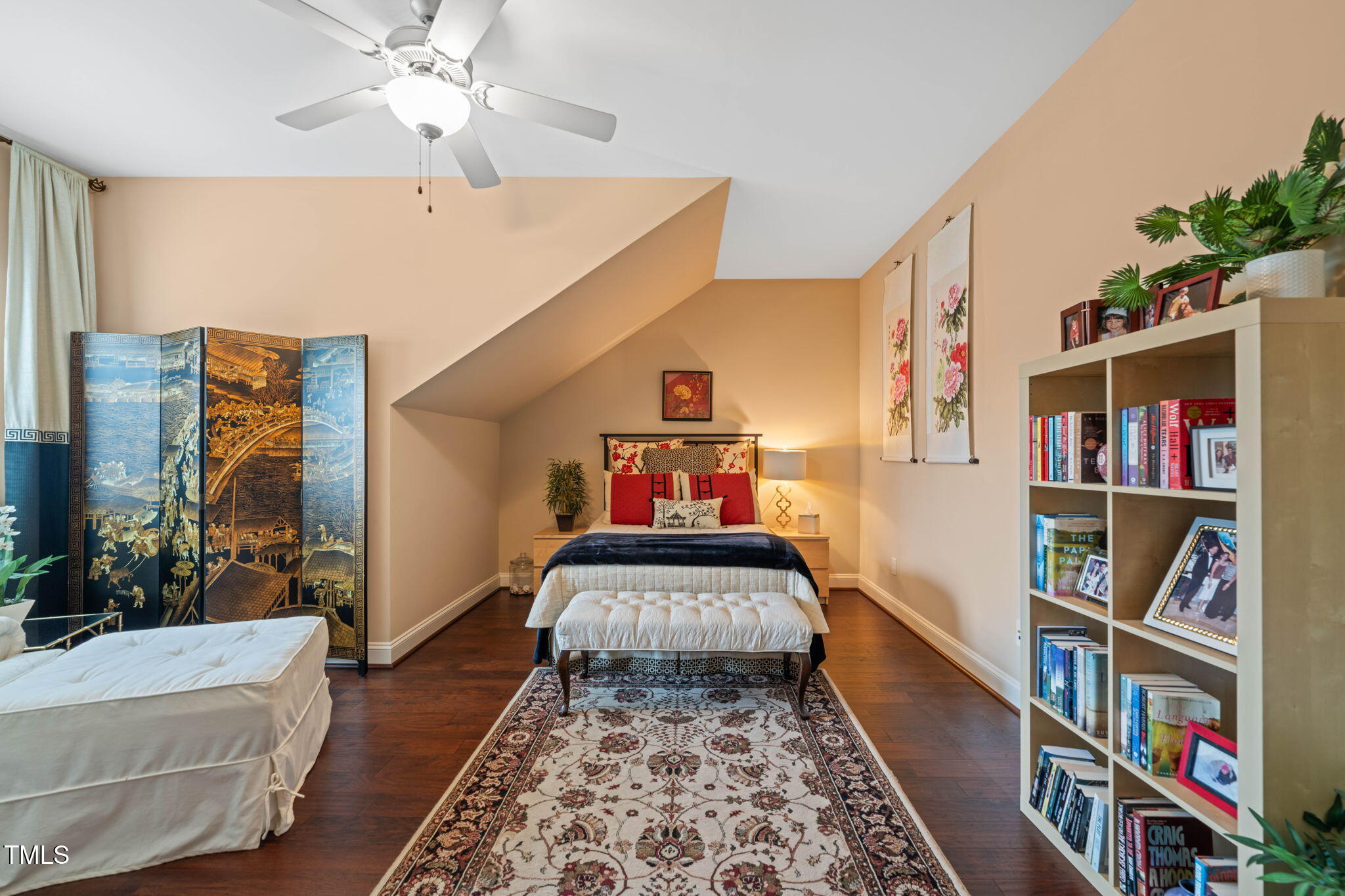 Furnished bedroom with a sloped ceiling, patterned rug, decorative screen, and bookcase.