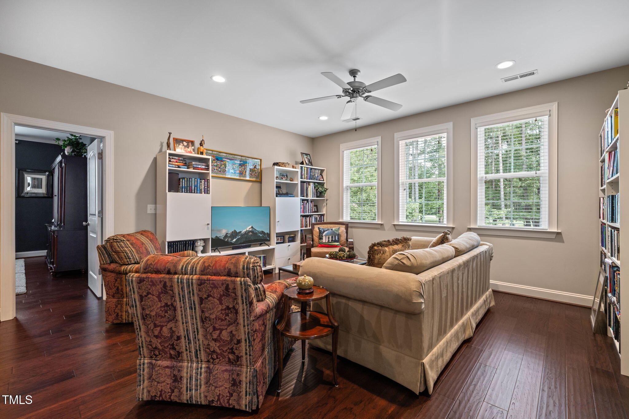 Living room with built-in bookshelves, three bright windows, patterned armchairs, and a beige sofa.