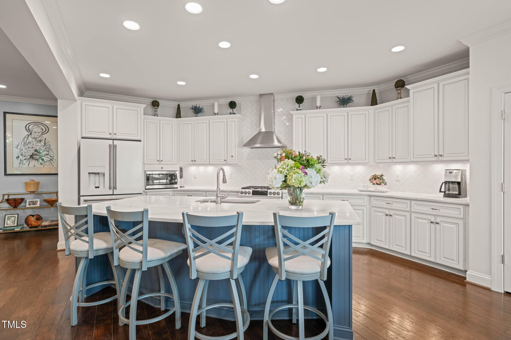 Kitchen with white cabinetry, a blue seating island, stainless steel appliances, and dark hardwood floors.