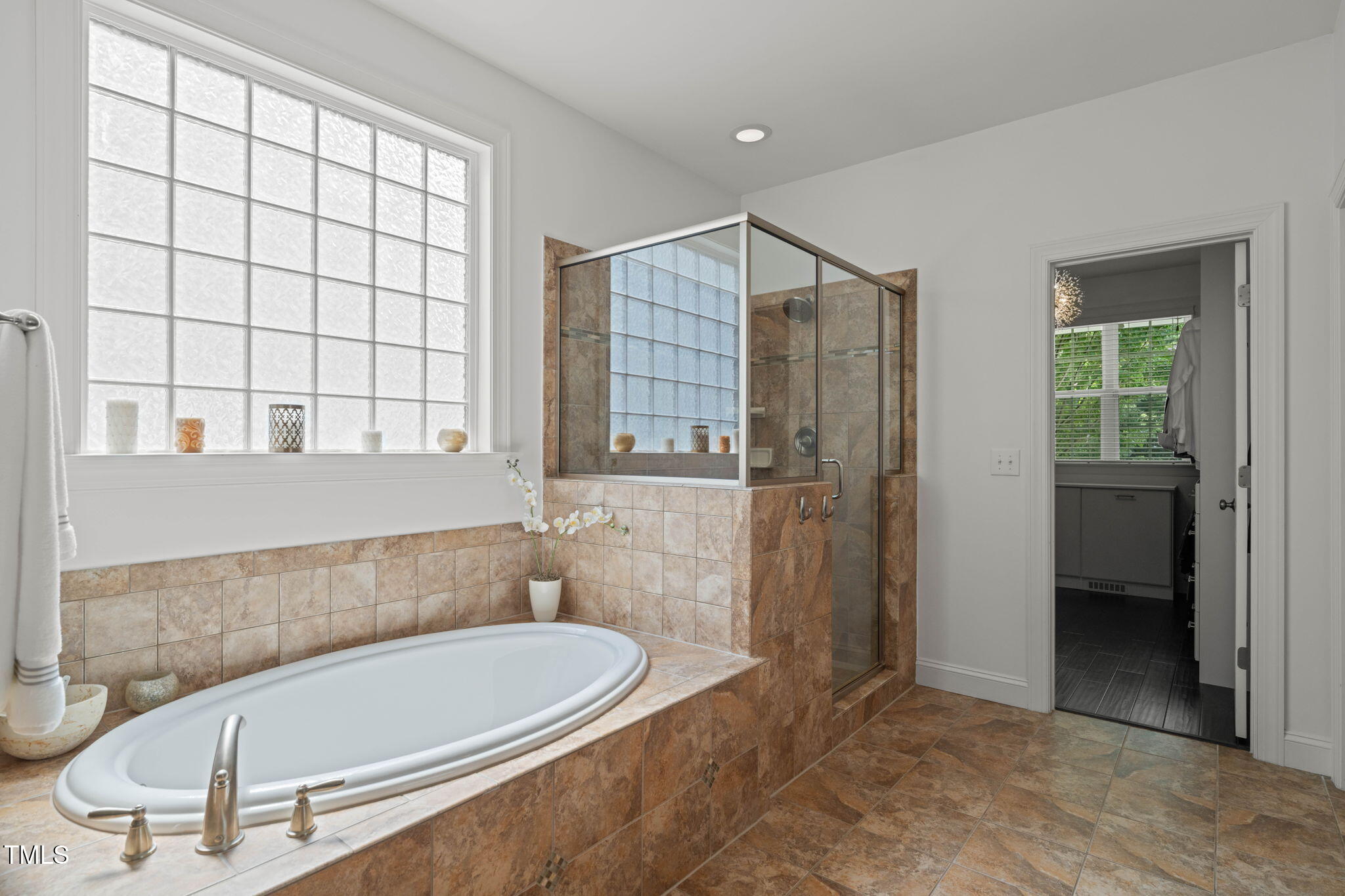 Bathroom with a tiled soaking tub, glass-enclosed shower, and large grid-pane window.
