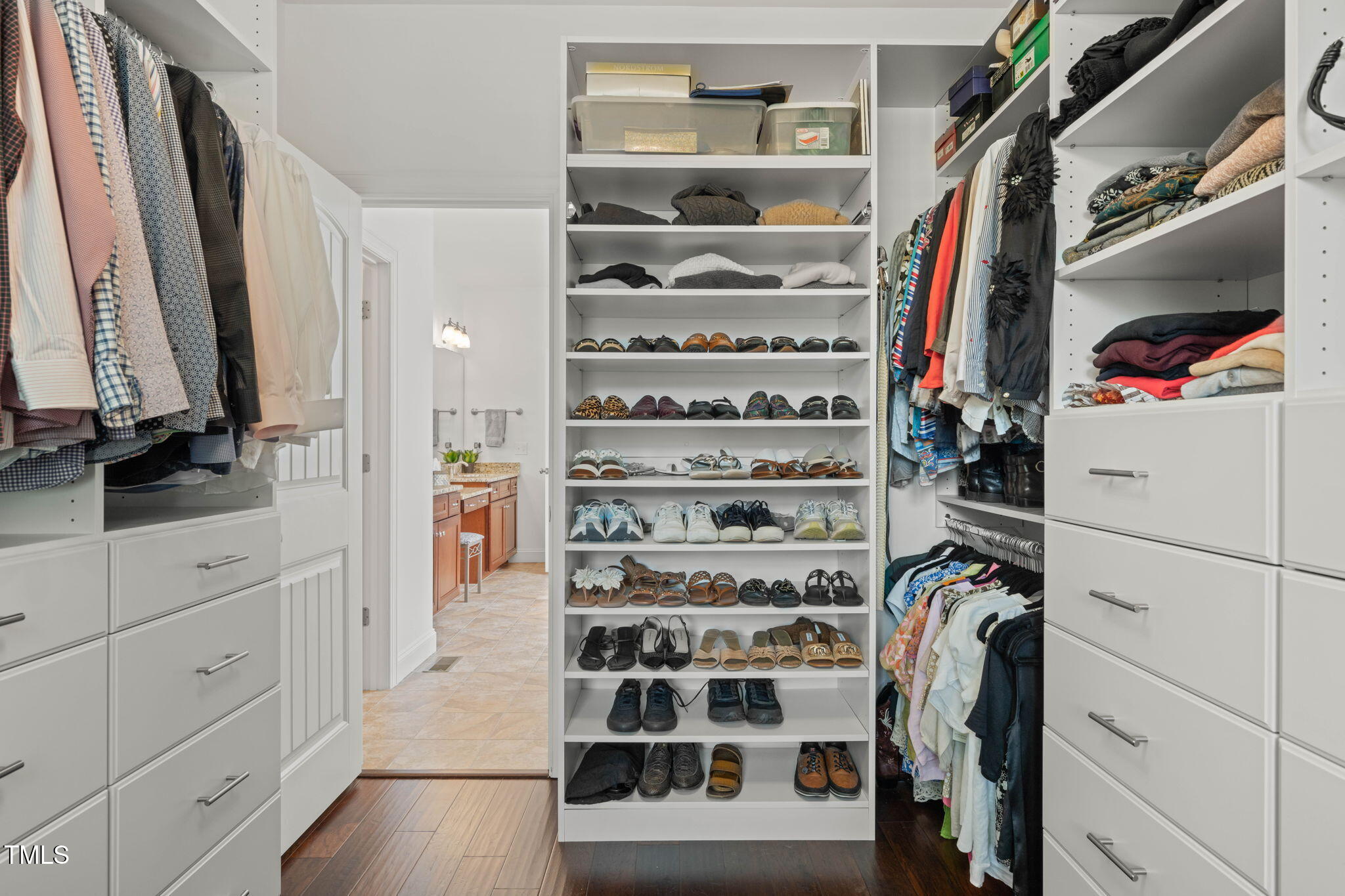 Walk-in closet with built-in drawers, hanging clothes, and shelves of shoes.