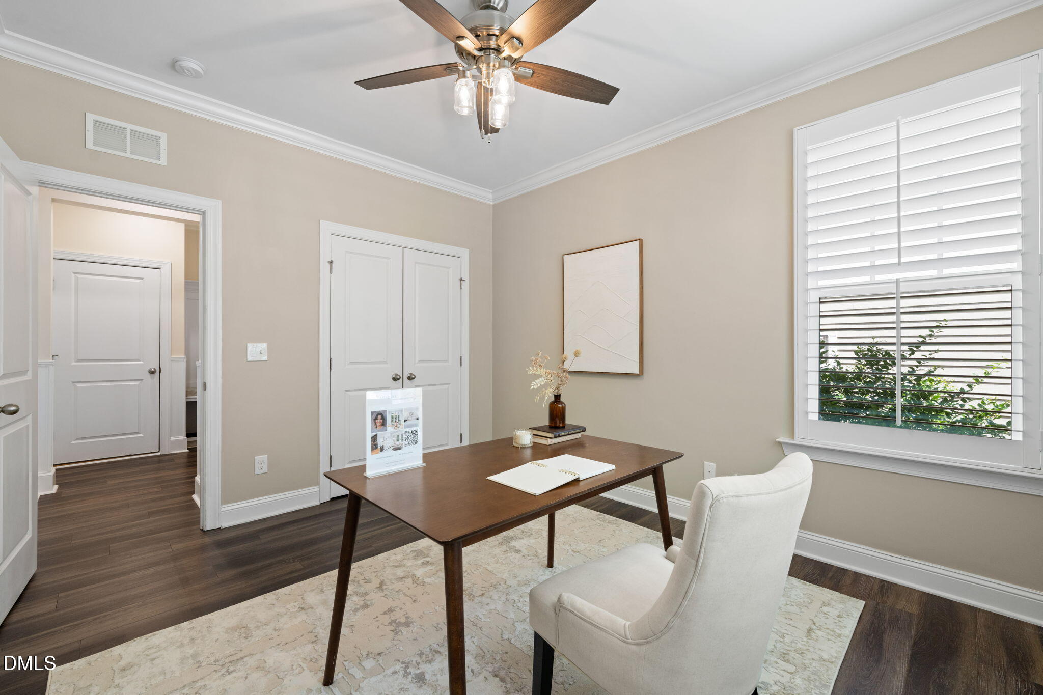 Furnished home office with a dark wood desk, white chair, and shuttered window.