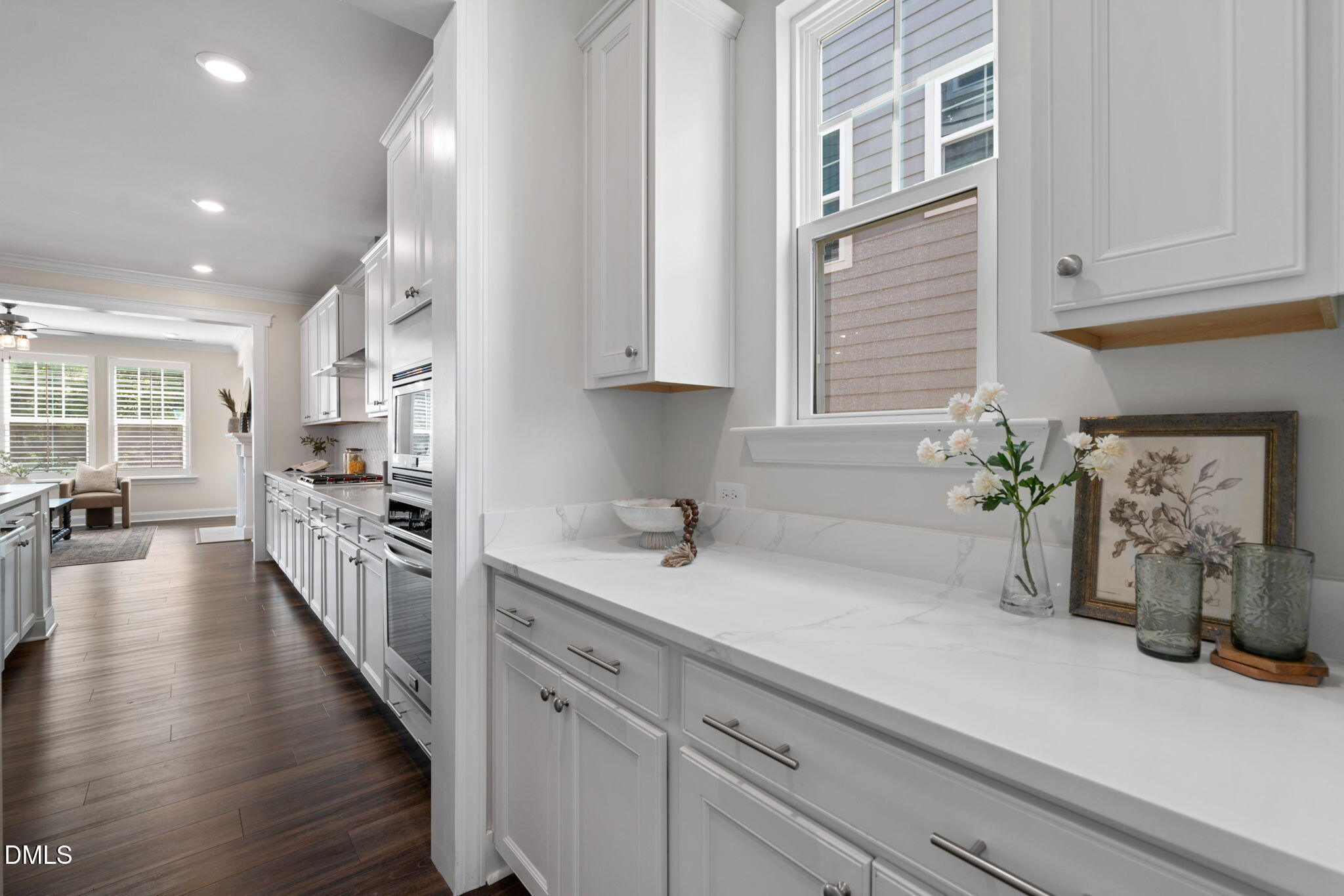 Bright white kitchen with marble-look counters, stainless appliances, and dark wood floors.