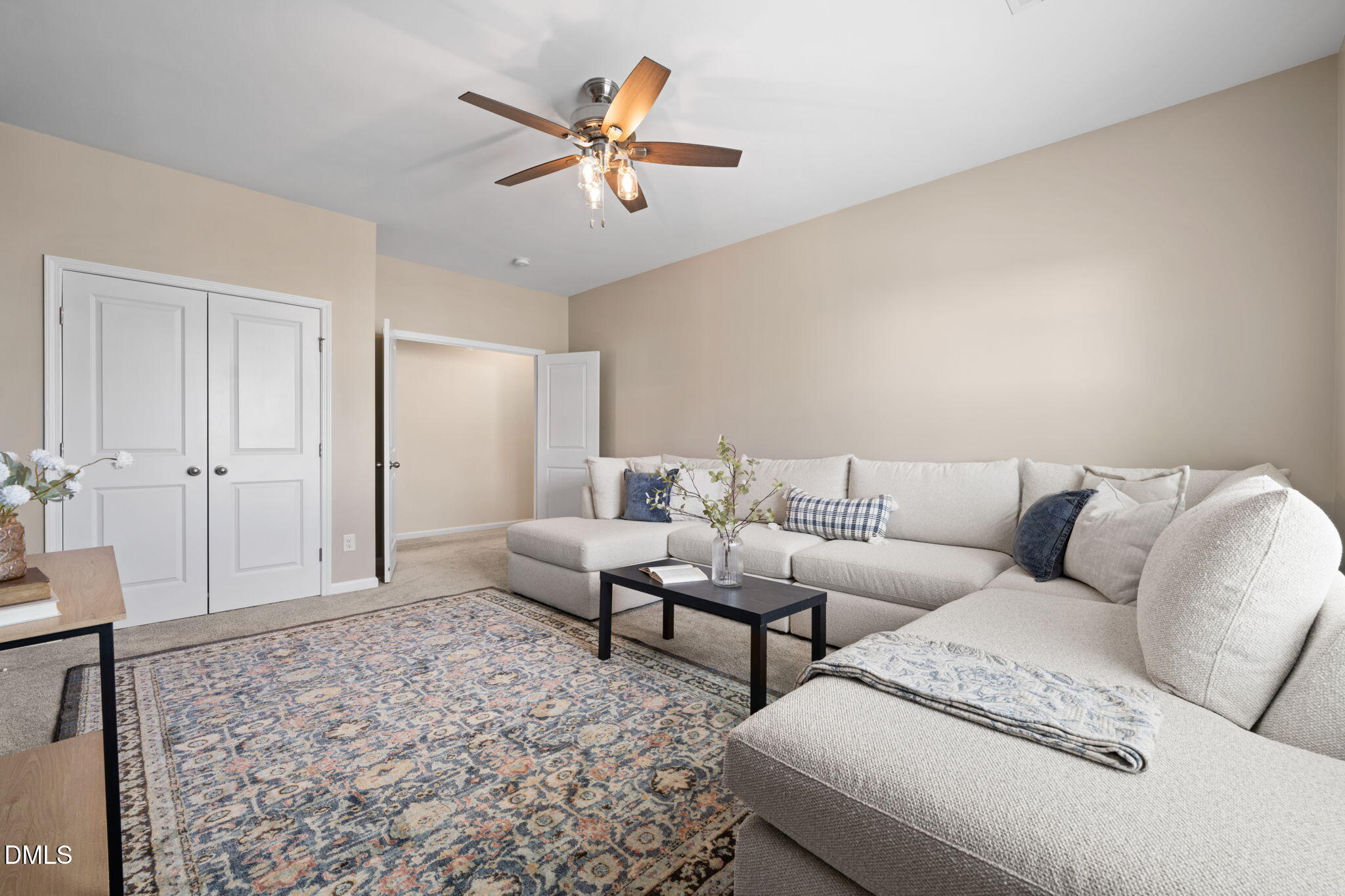 Living room with a light sectional sofa, patterned rug, and ceiling fan.