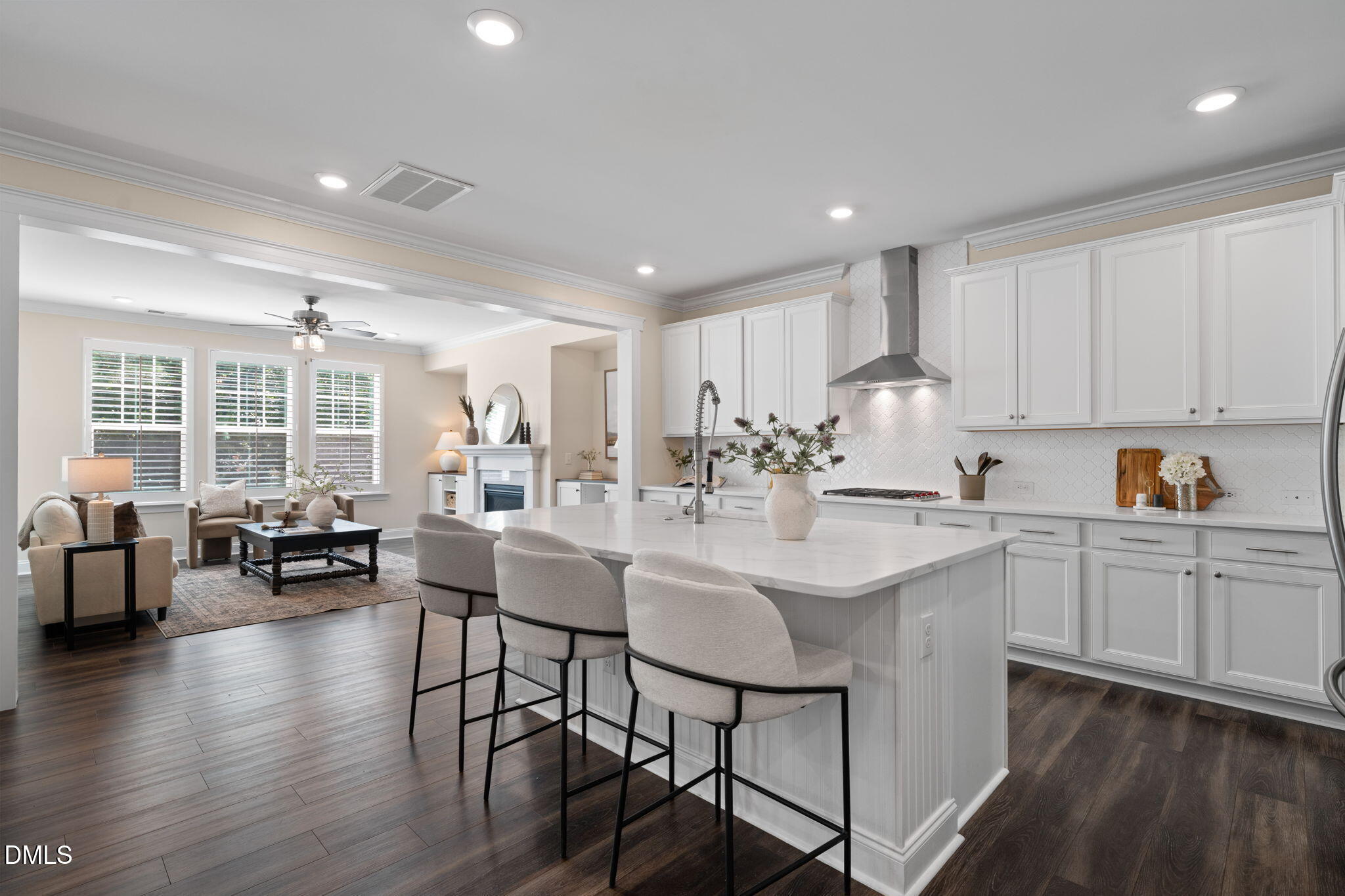 Open-plan kitchen with a large white island and three bar stools beside a living area with a fireplace.