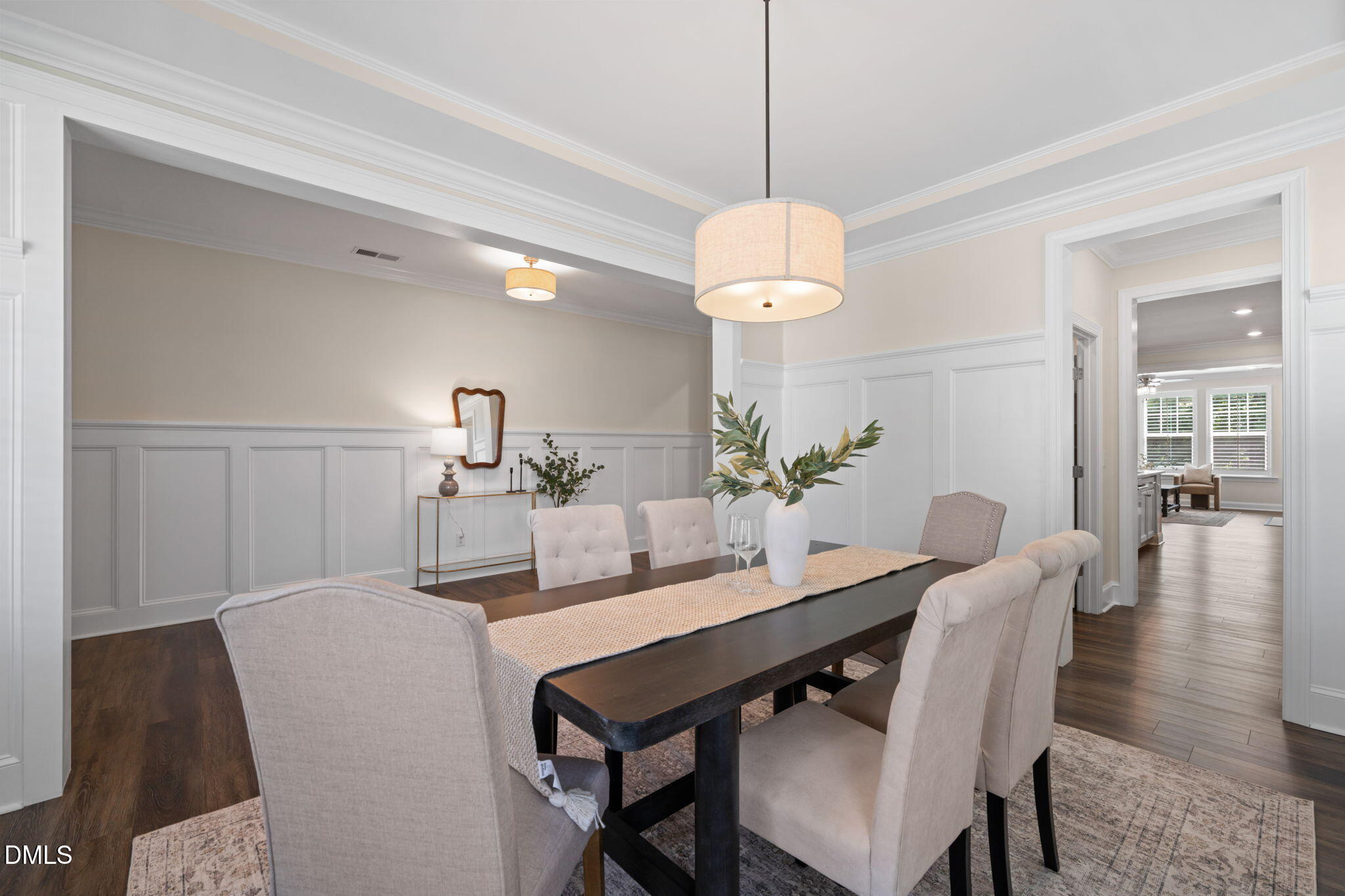 Staged dining room with paneled walls, upholstered chairs, and an open doorway to a bright sitting area.
