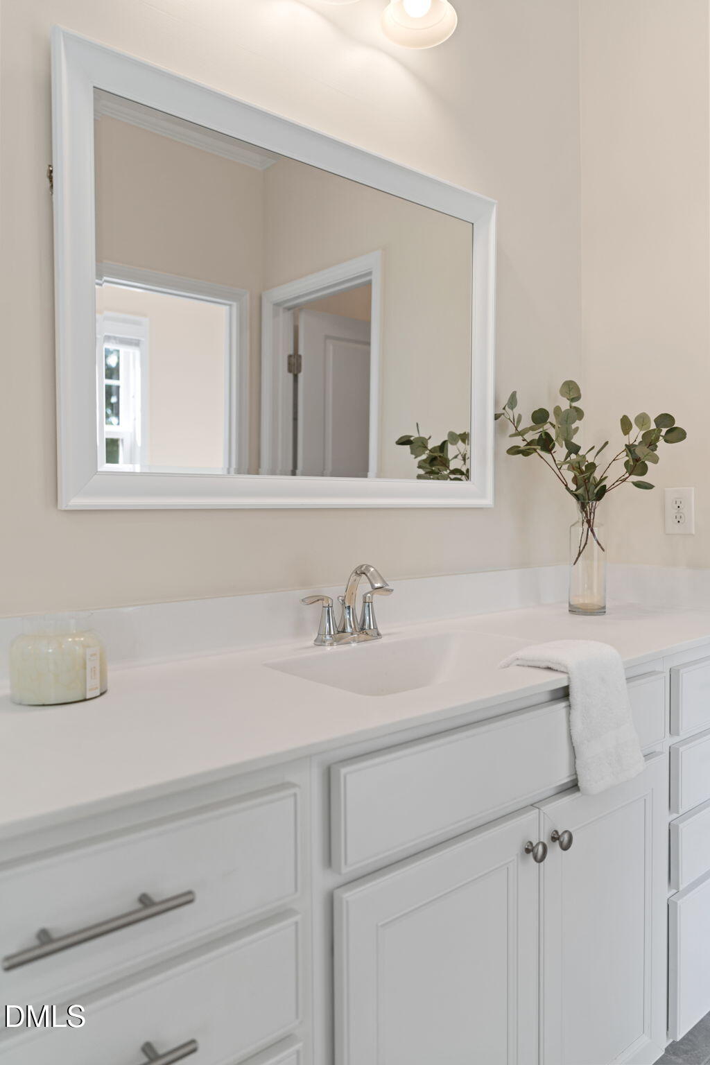 Bathroom vanity with white cabinetry, a large framed mirror, and greenery beside the sink.