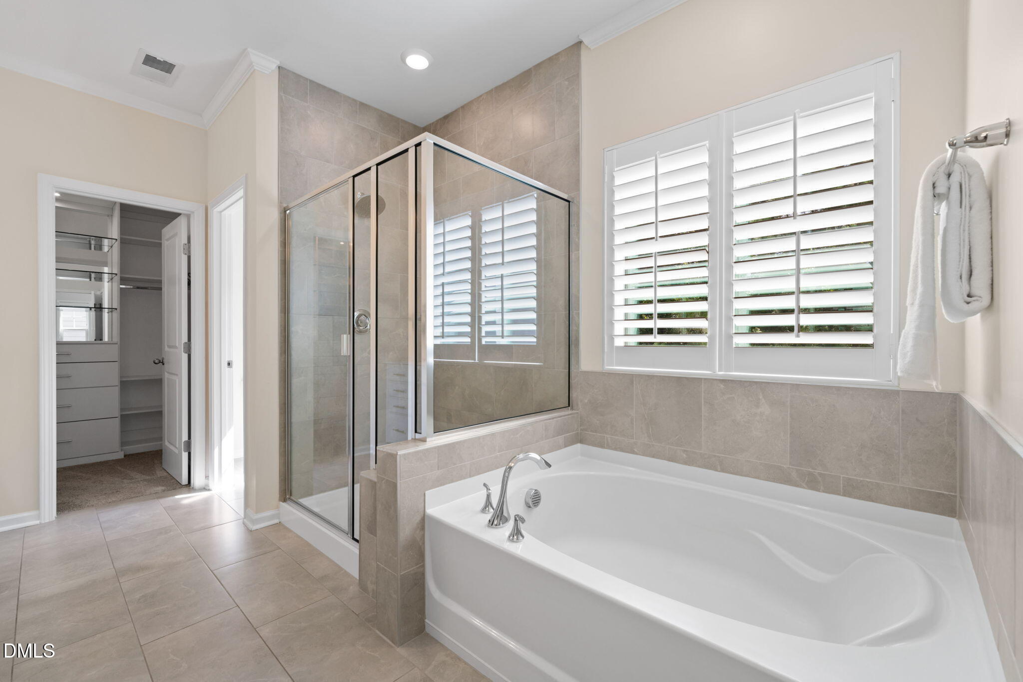 Bathroom with a large soaking tub, glass shower, and plantation-shuttered window.