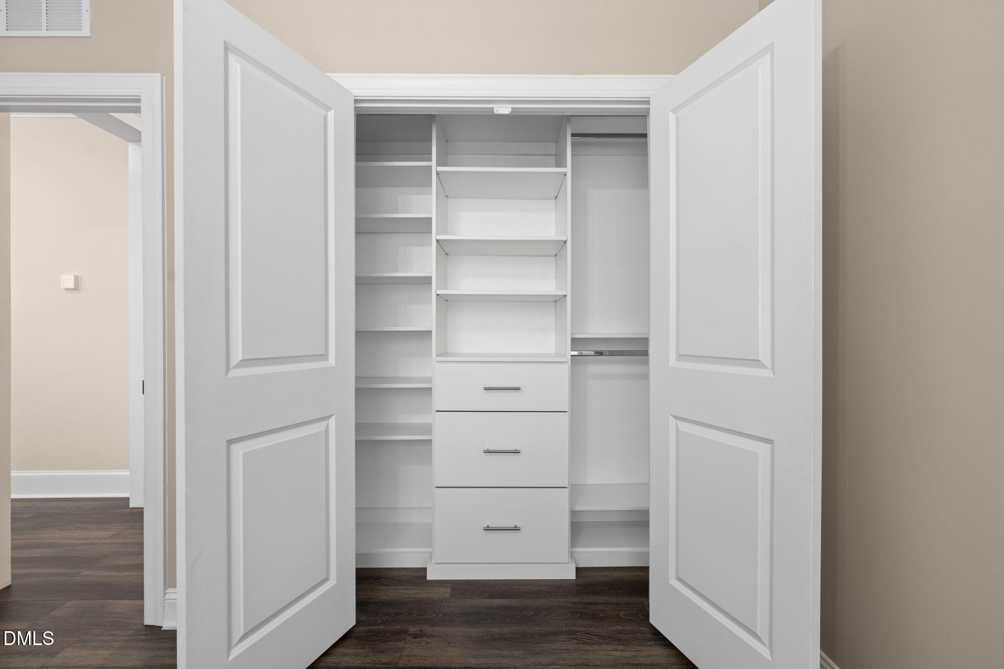 Walk-in closet with white built-in shelves and three central drawers.